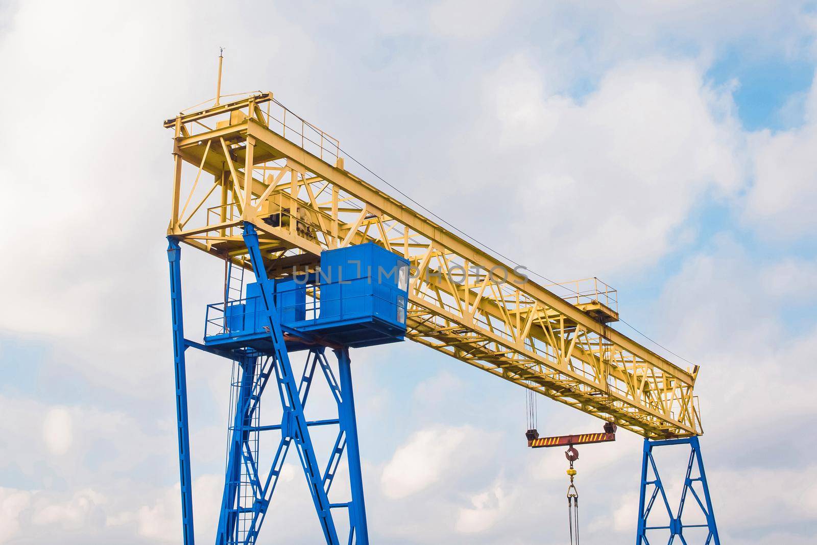 Overhead industrial hoisting crane on a background of blue sky with clouds.