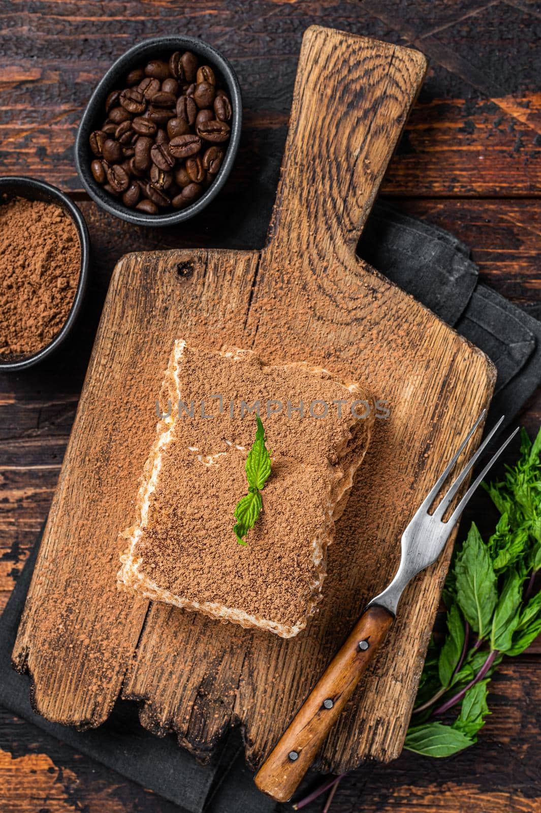 Italian dessert Tiramisu cake with cocoa and mint on a wooden board. Dark Wooden background. Top view by Composter
