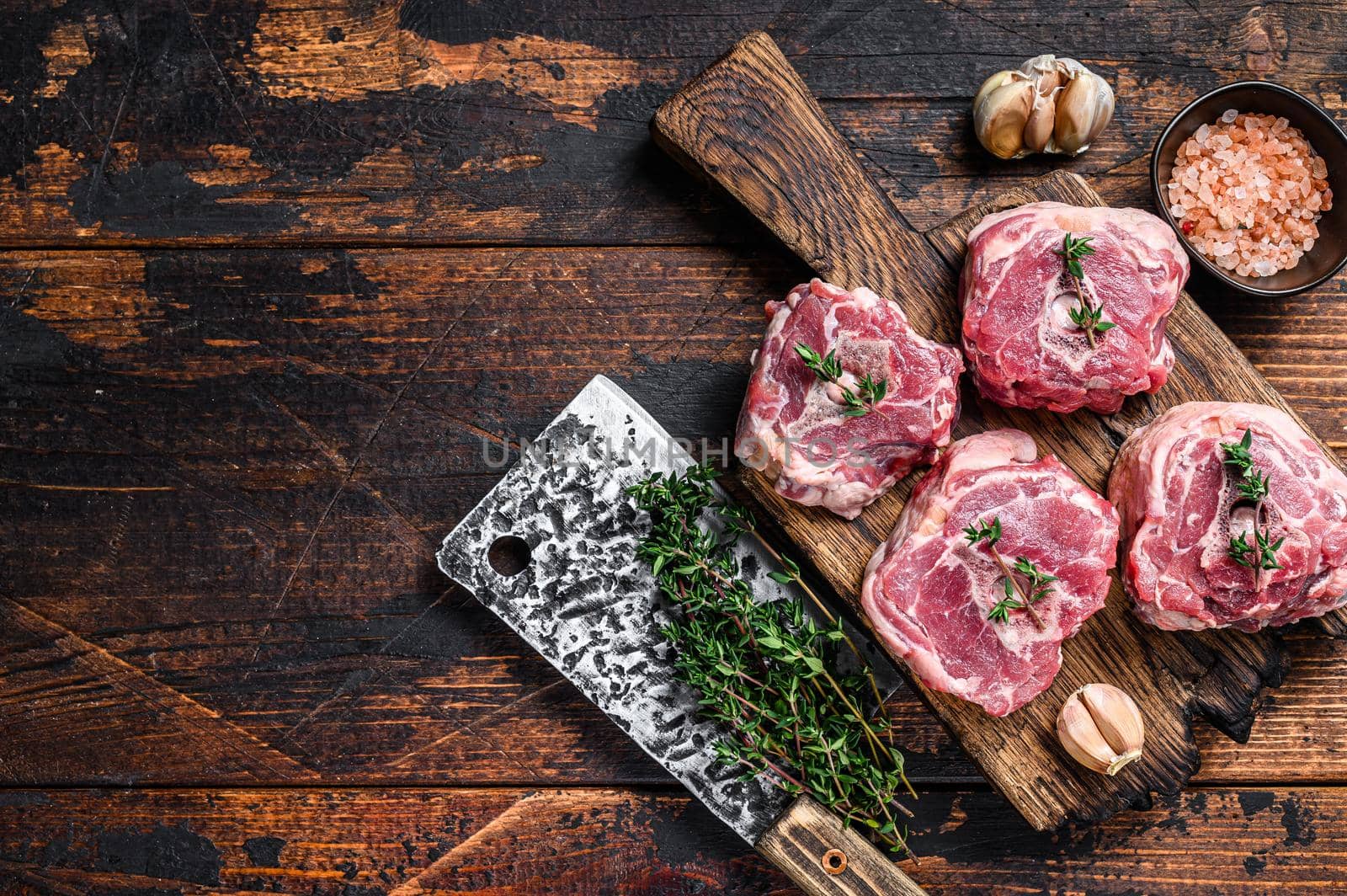 Raw mutton lamb neck meat on a butcher board with cleaver. Dark wooden background. Top view. Copy space by Composter