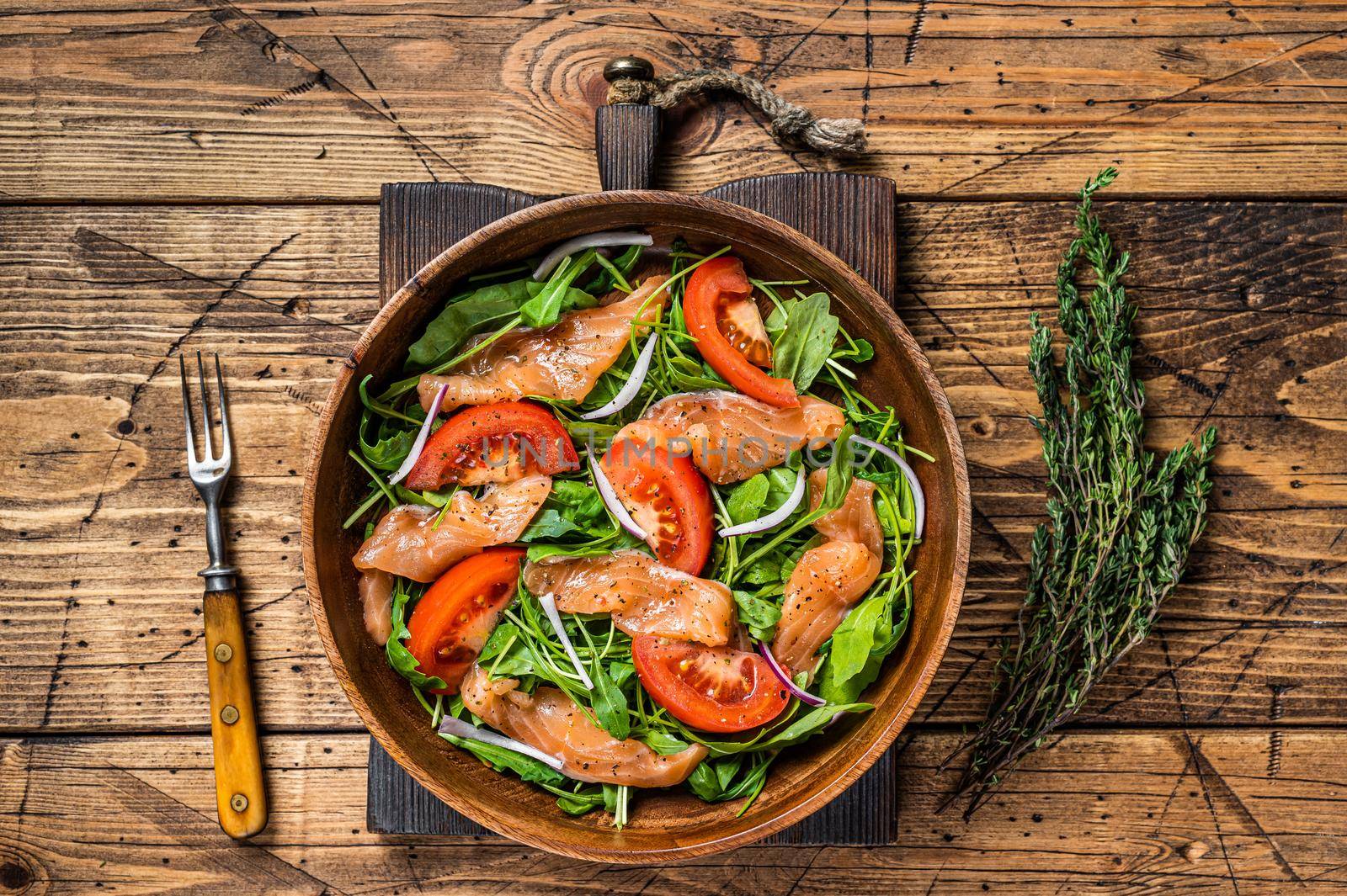 Vegetable salad with smoked salmon, arugula, tomato and green vegetables. wooden background. Top View.