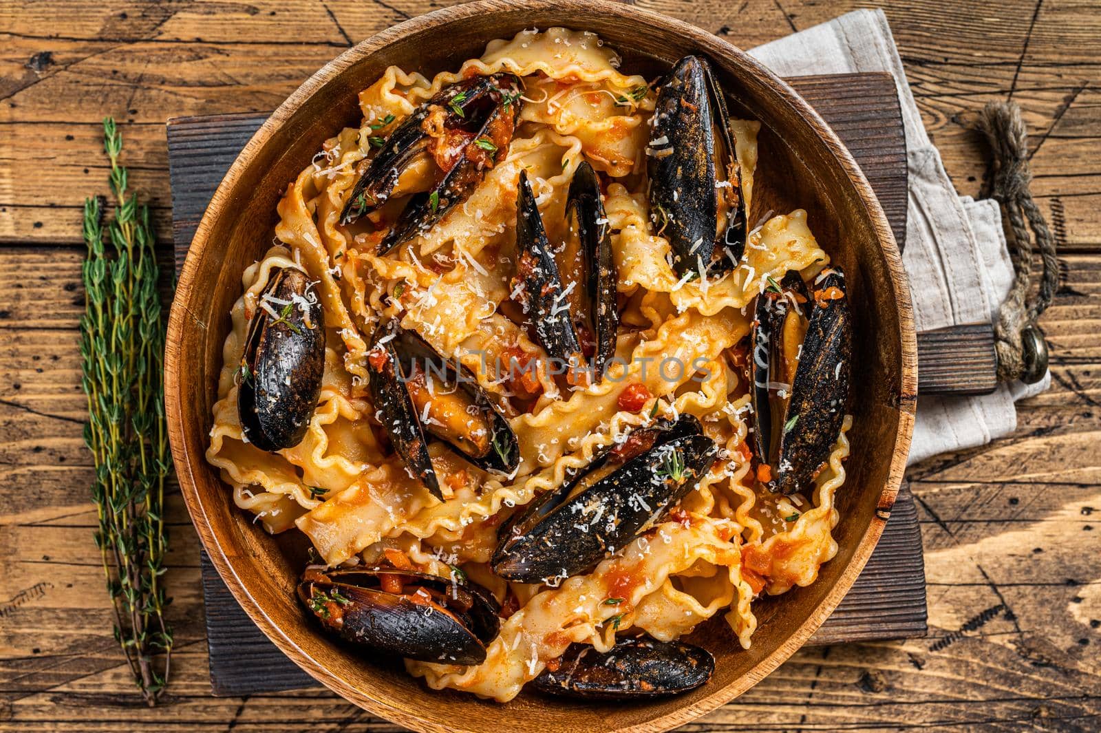 Mussels and clams Mafaldine pasta with tomato sauce in a rustic wooden plate. Wooden background. Top view by Composter