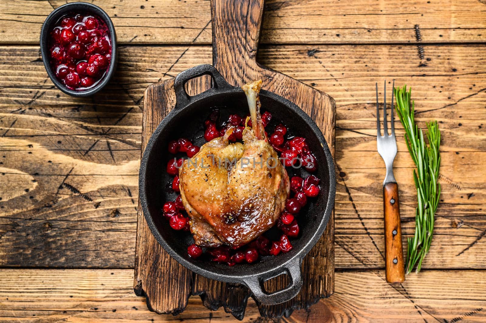 Fried duck leg with cranberrie sauce in a pan. wooden background. top view by Composter