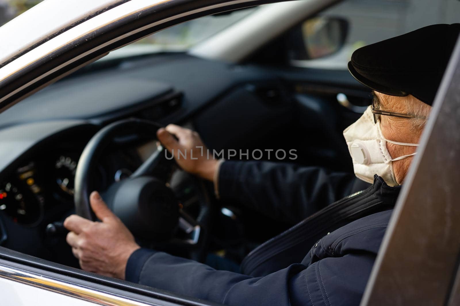 Elderly man wearing face mask entering his car at home. by Andelov13