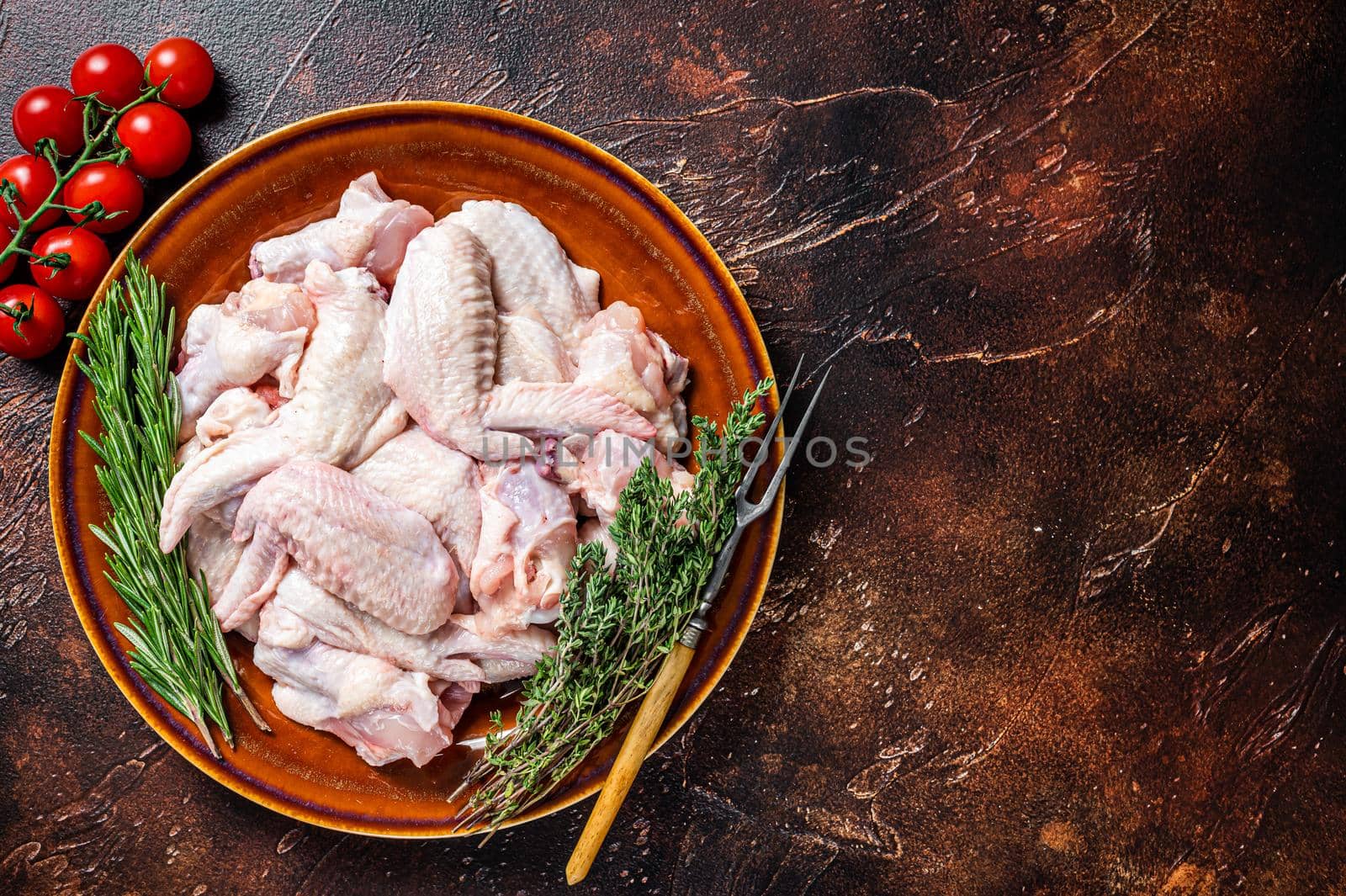 Cut Raw chicken wings in a rustic plate with thyme and rosemary. Dark background. Top view. Copy space by Composter