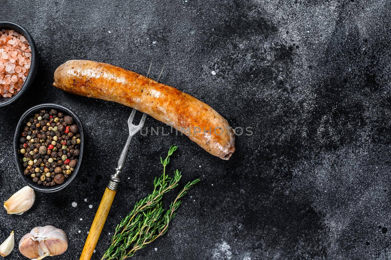 Pork Sausage bbg grilled with spices and herbs on a meat fork. Top view. Black background. Copy space by Composter