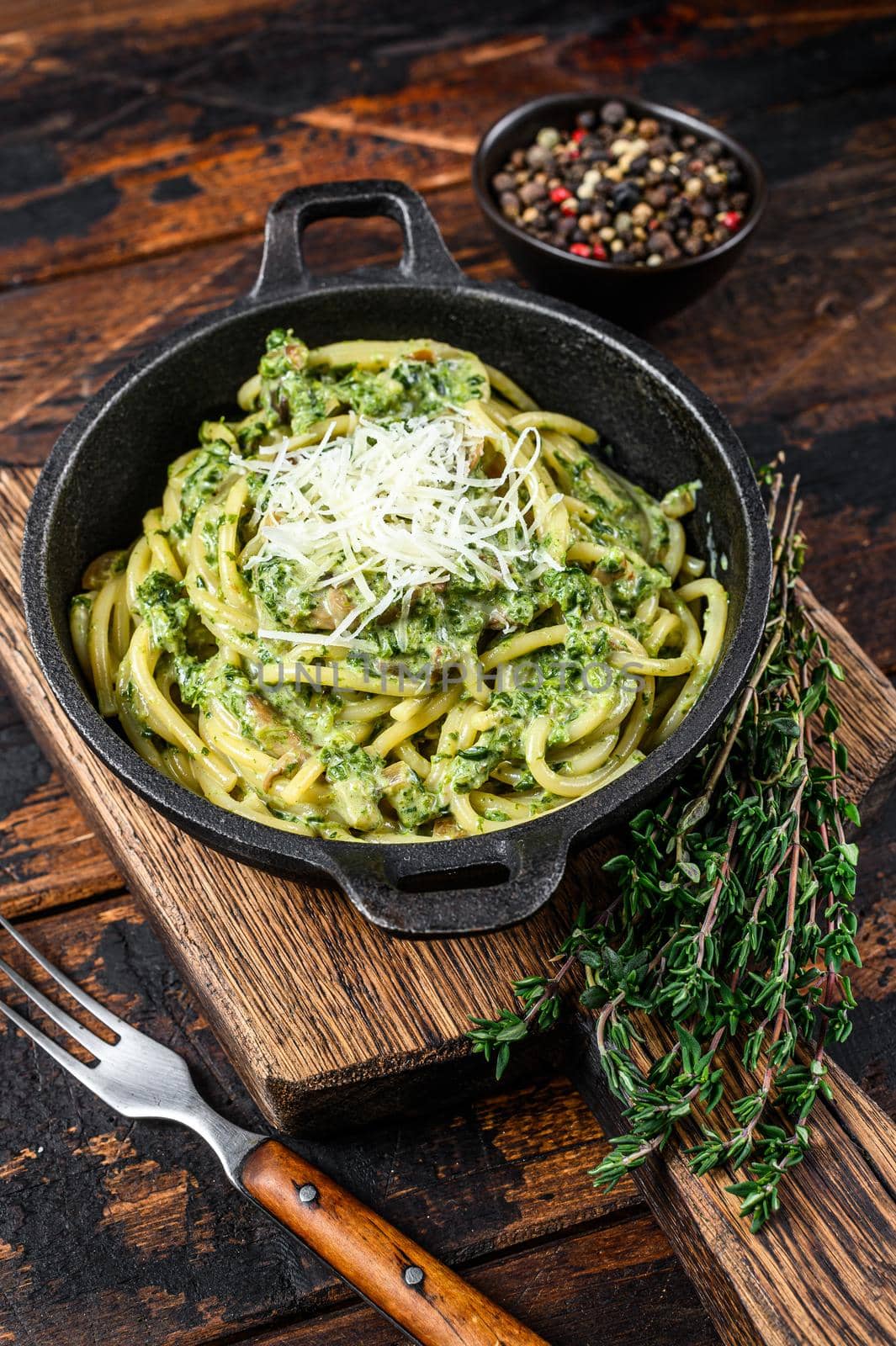 Spaghetti Pasta with pesto sauce, spinach and parmesan in a pan. Dark Wooden background. Top view.