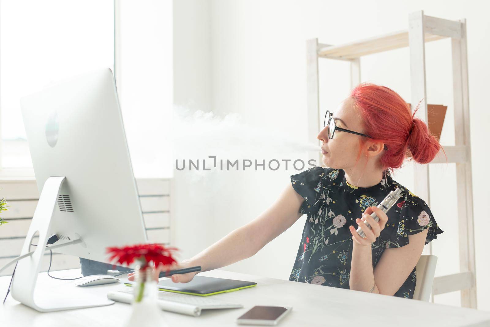 Creative, graphic designer, people concept - young creative woman smoking a vape while working in a graphic tablet.