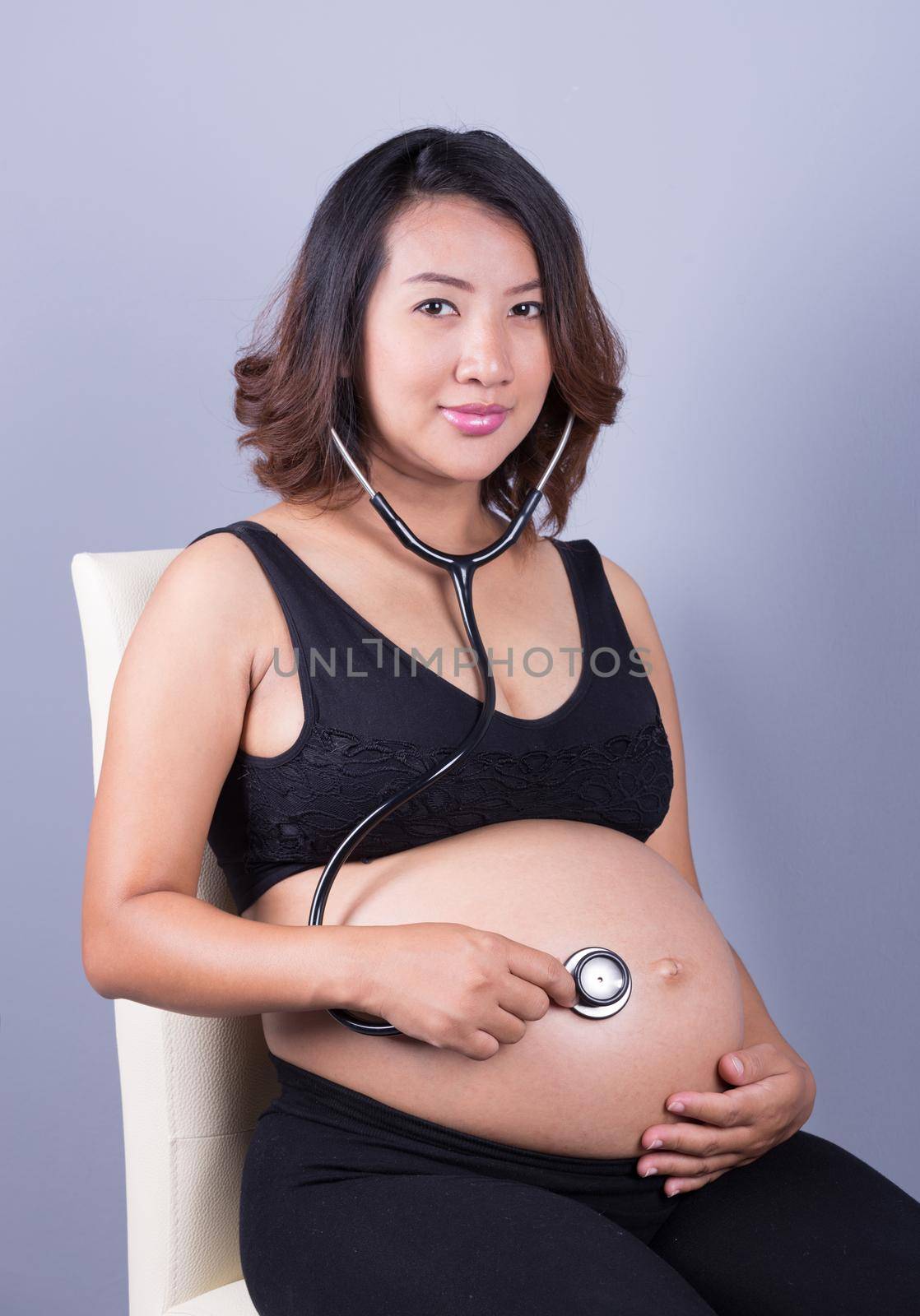 young pregnant asian woman with stethoscope listening belly to baby by geargodz