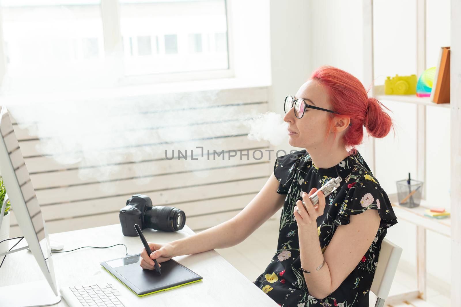 graphic designer concept - Female graphic designer working on computer while using graphic tablet at desk in the office and smoking a vape.