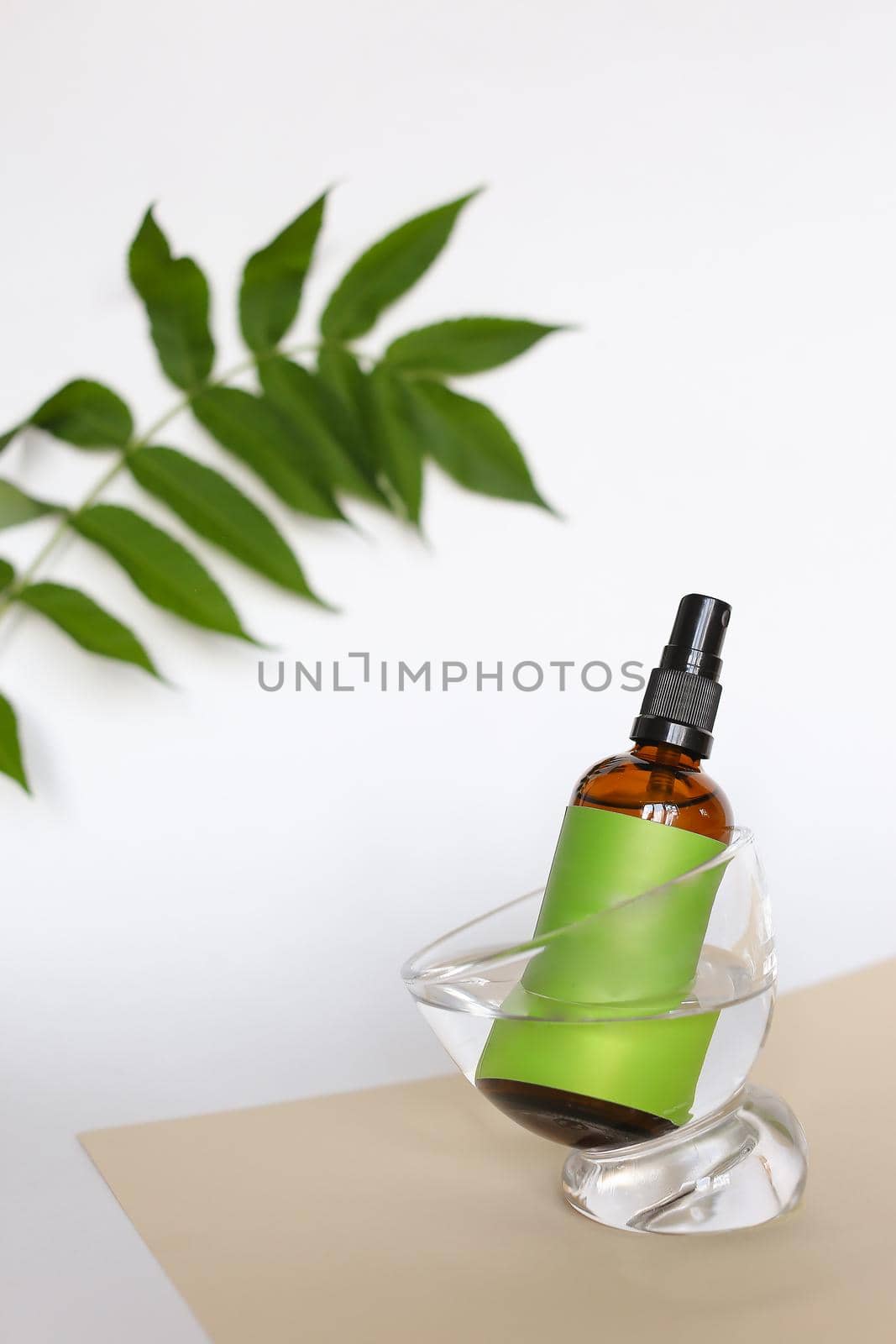 Close up brown glass bottle with cosmetic product and green space for brand on white background with leaf. Concept of cluelty free, organic, kosher cosmetics in online shop for skin and body.