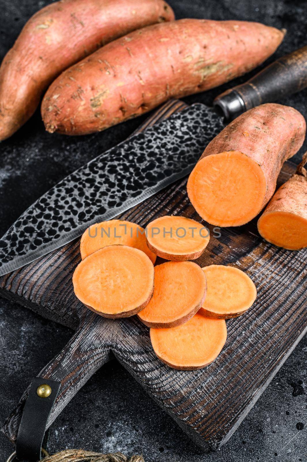 Raw cut batata Sweet potato on Wooden cutting board. Black background. Top view by Composter