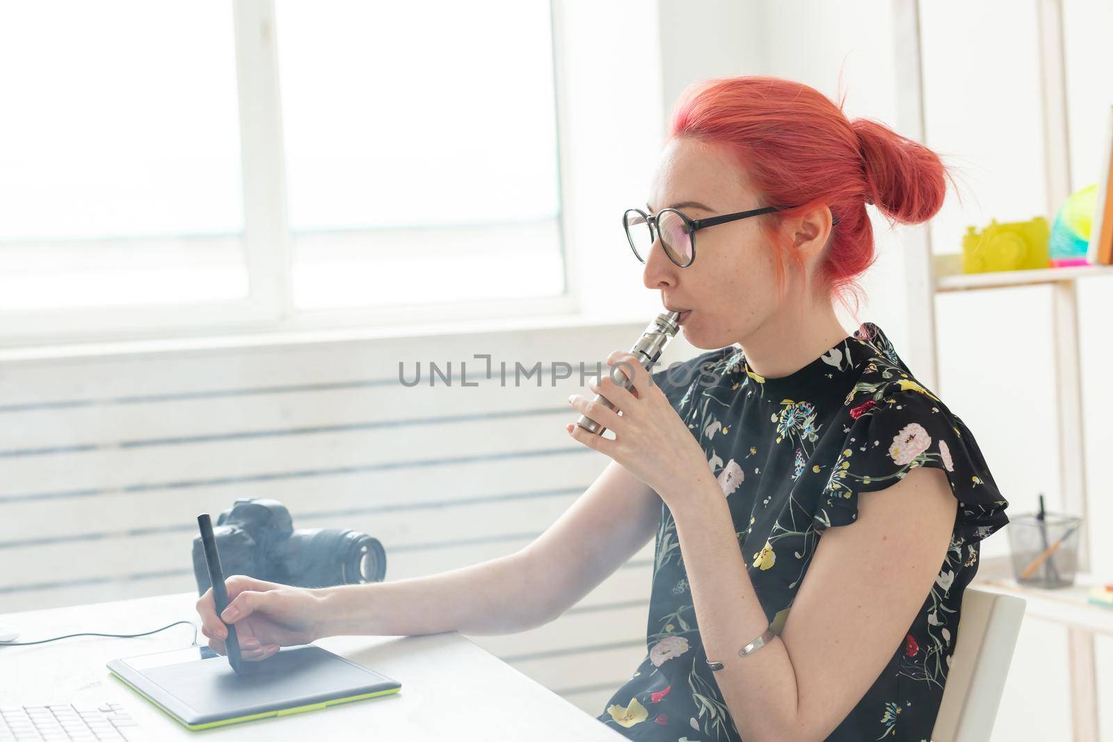 graphic designer concept - Female graphic designer working on computer while using graphic tablet at desk in the office and smoking a vape.