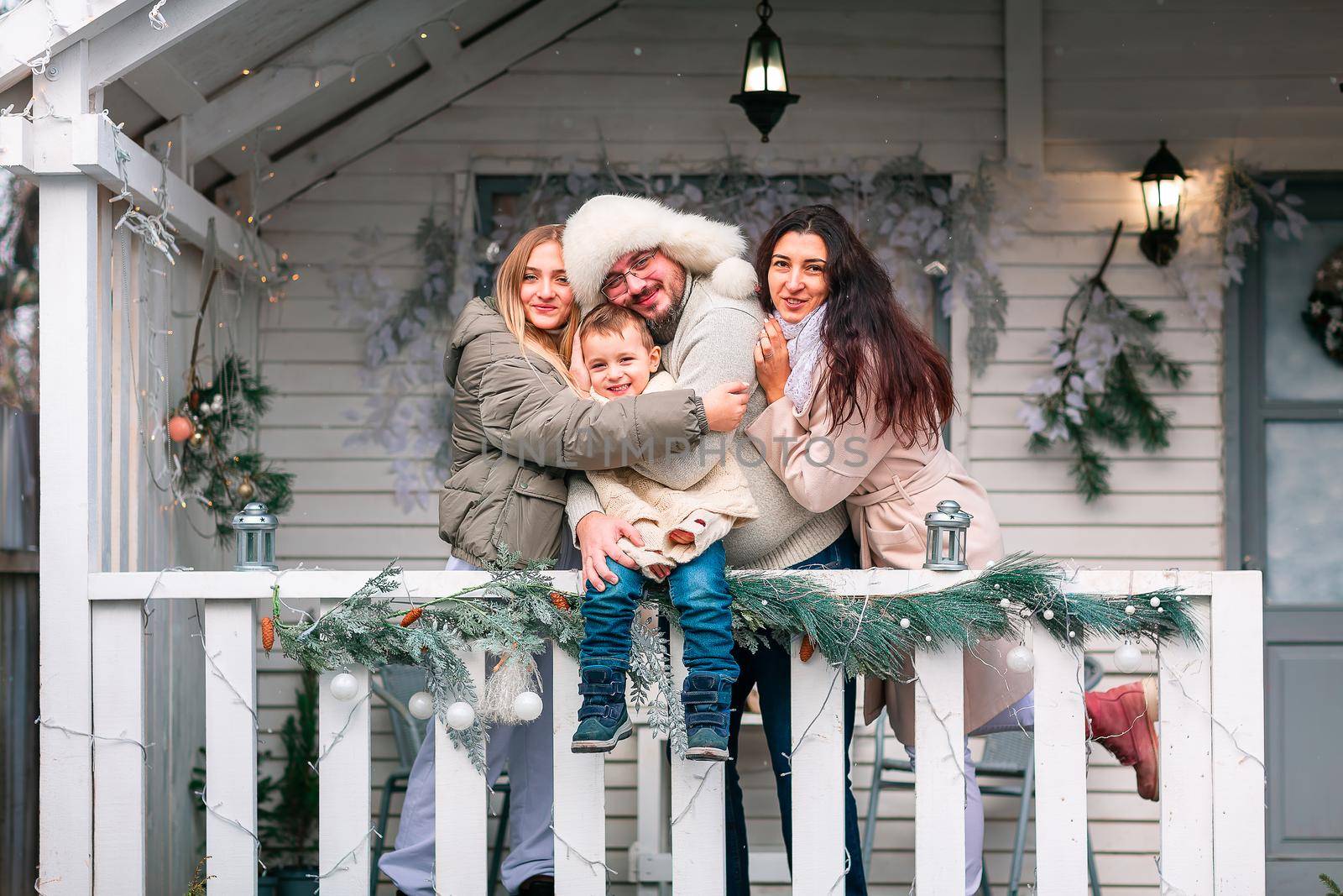 Happy family on the porch of the Christmas decorated house, snowing outdoor. Happy New Year and Merry Christmas. Magic winter