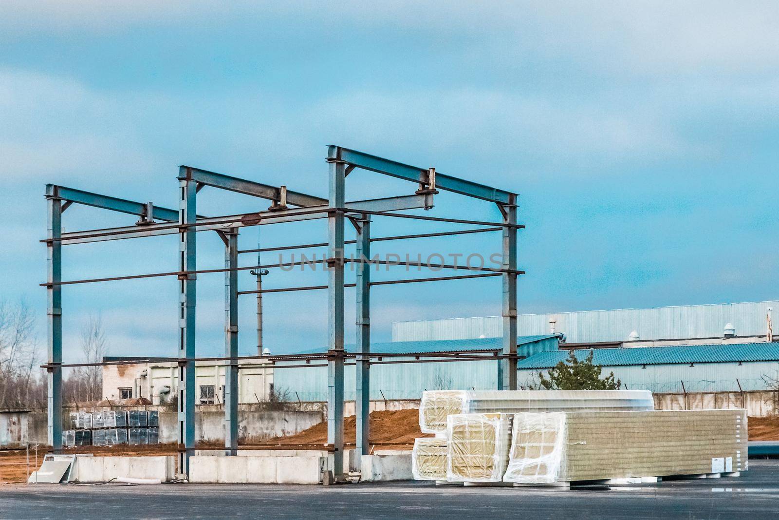 Metal frame of a new modern building under construction and packed sandwich panels at a construction site by AYDO8