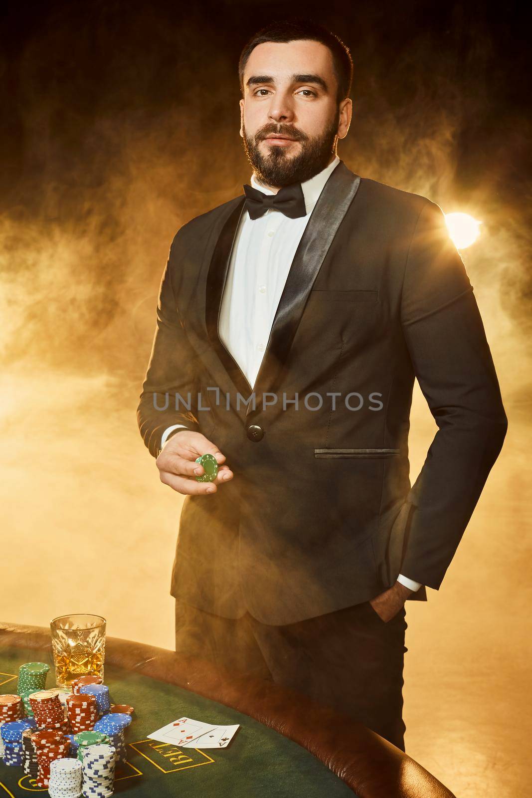 A young man in a business suit standing near poker table. Man gambles. The player at the gaming table playing cards.