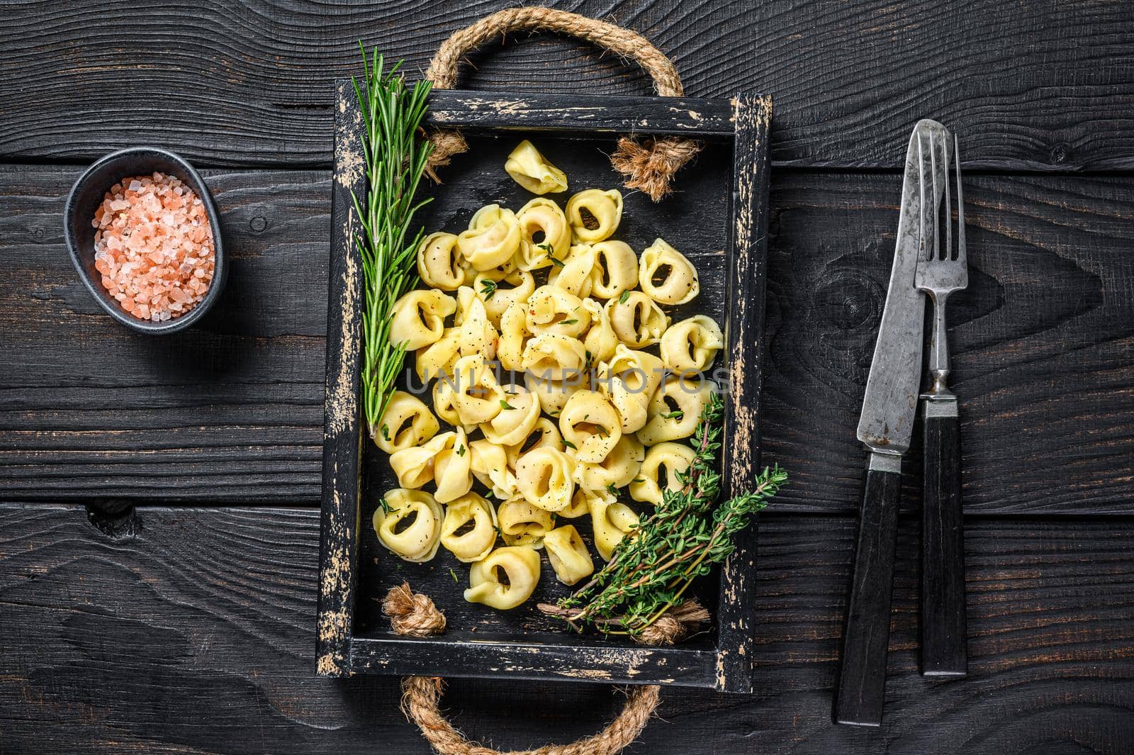 Italian traditional tortellini pasta with spinach in a wooden tray. Black wooden background. Top view.