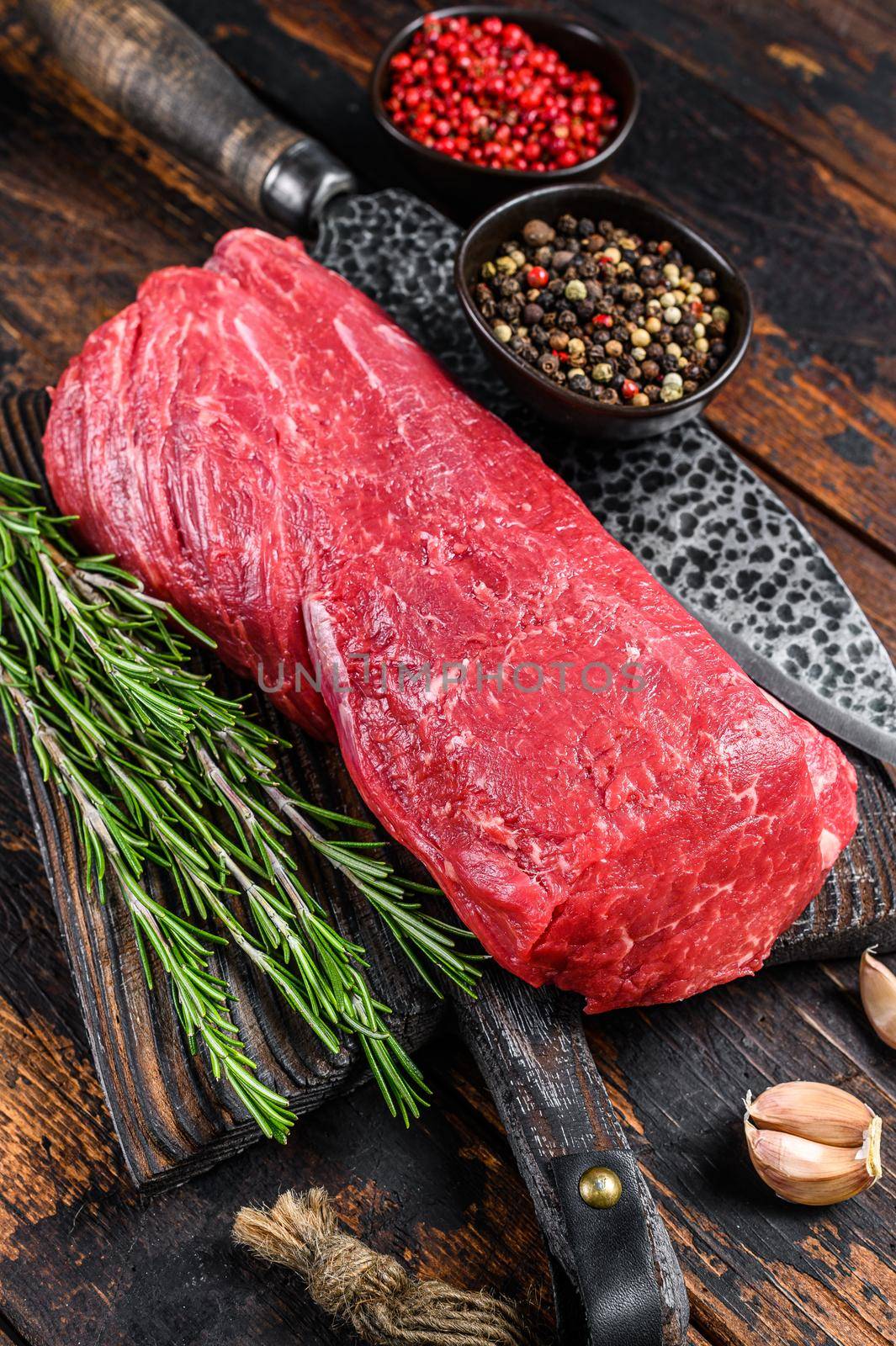 Whole Raw Tenderloin beef meat for steaks fillet mignon on a wooden cutting board with butcher knife. Dark wooden background. Top view.