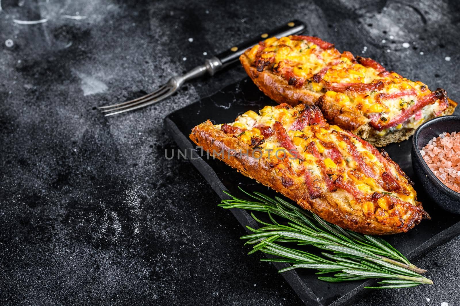 Hot baked open Baguette sandwich with ham, bacon, vegetables and cheese. Black background. Top view. Copy space by Composter