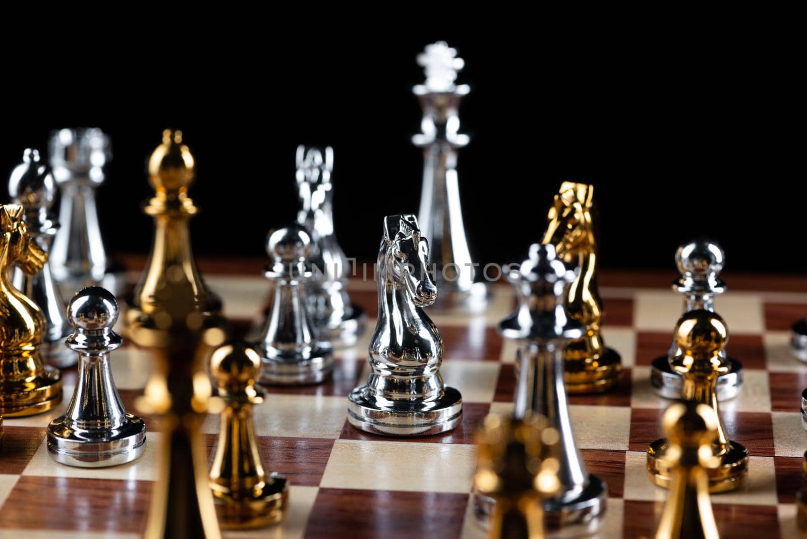 Gold and silver chess figures standing on chessboard. Intellectual and tactic game. Strategy planning, leadership and teamwork business concept. Close-up metal chess pieces on black background.