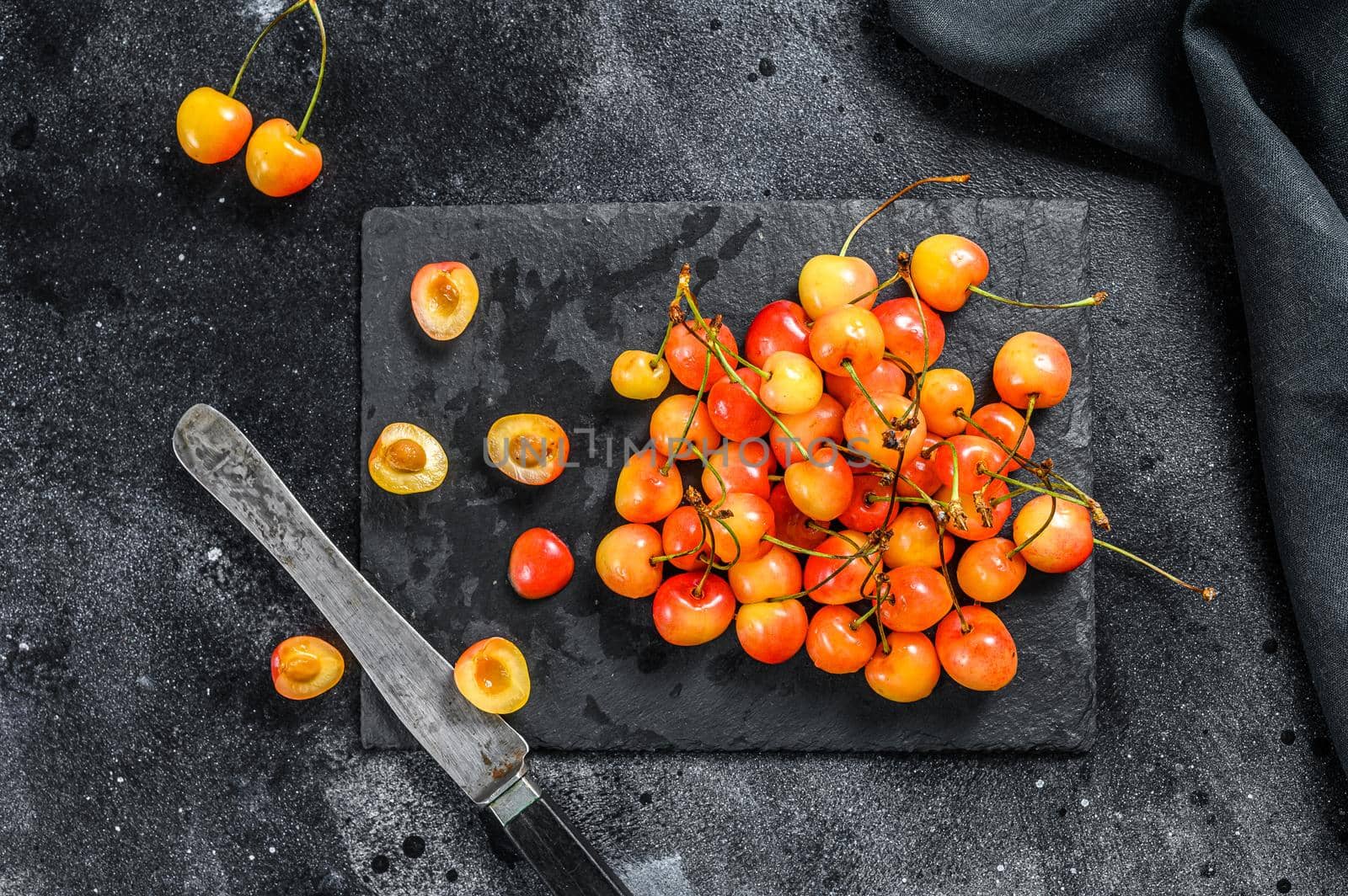 Yellow ripe cherries on a black plate. Black background. Top view.