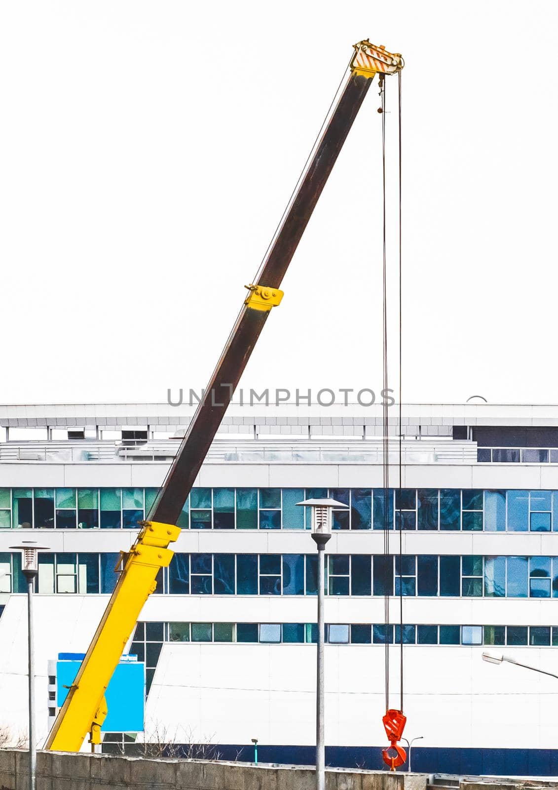 Machine lifting crane industrial equipment at a construction site on the background of a new, modern facade of an urban building by AYDO8