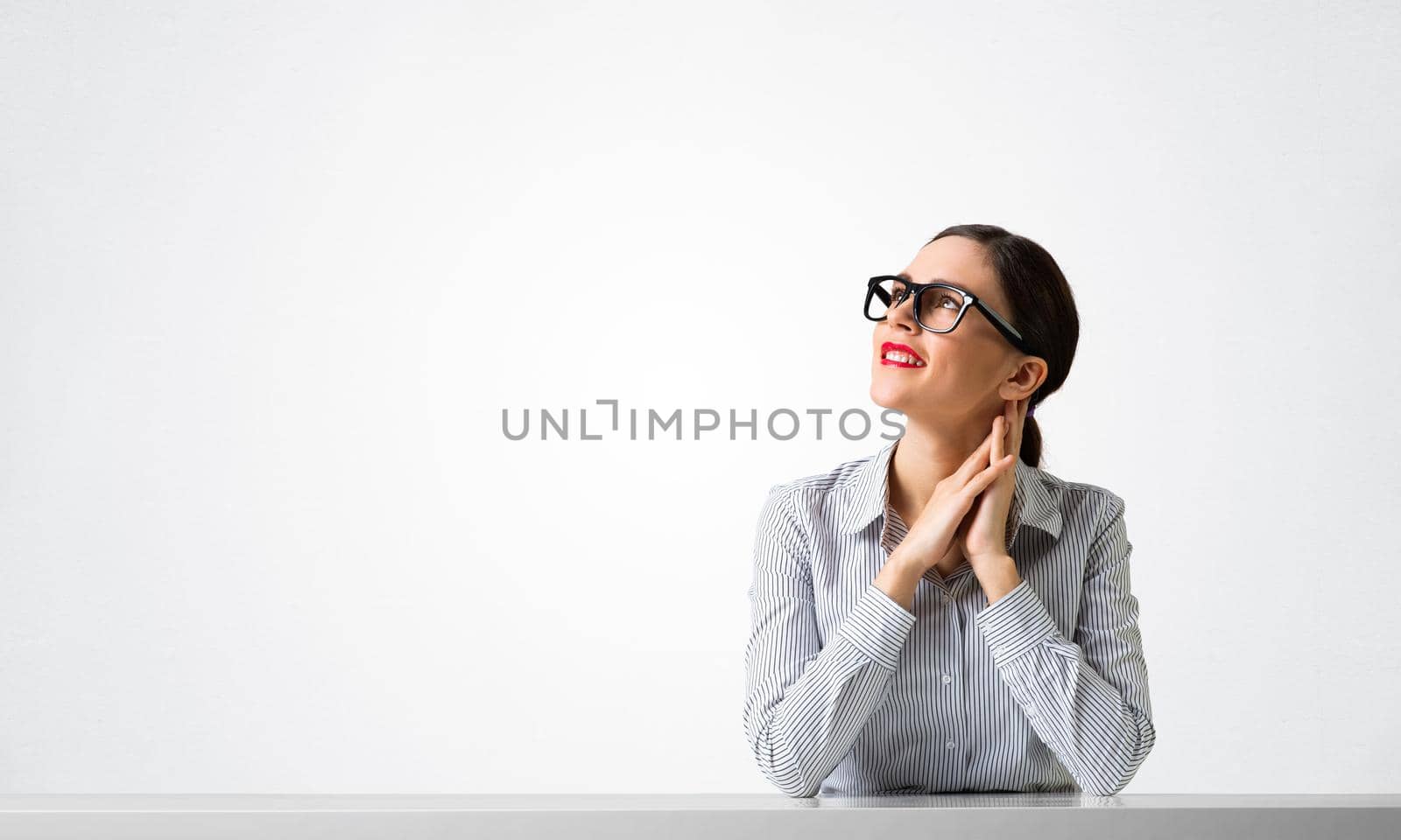 Confident businesswoman sits at desk and looking away. Young student has serious facial expression. Portrait of beautiful girl in glasses. Human resource and career development concept with copy space