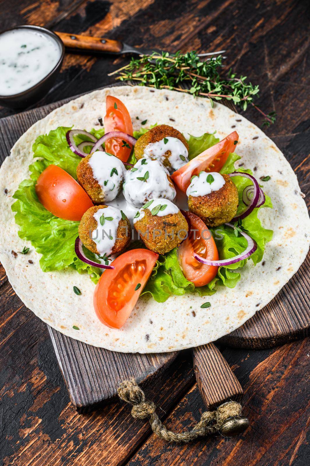 Vegetarian falafel with vegetables and tzatziki sauce on a tortilla bread. Dark wooden background. Top view.