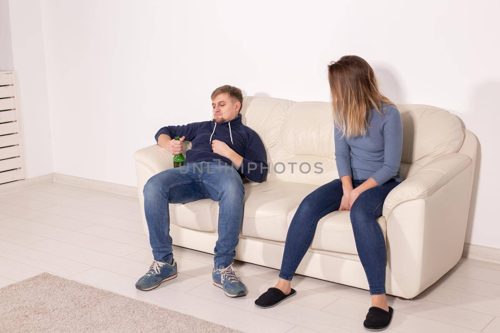 Alcoholism, abuse and domestic violence concept - sad woman sitting on sofa with drunk husband.