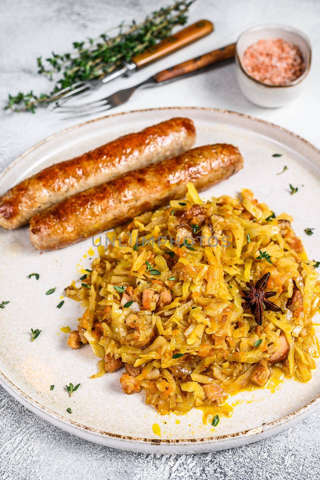 Stewed cabbage with mushrooms and meat sausages on a plate. White background. Top view.