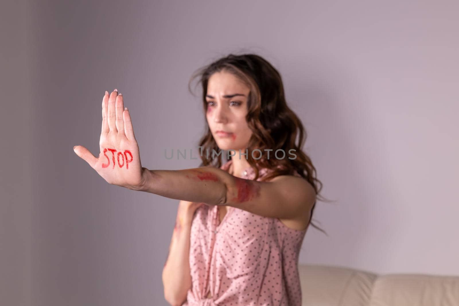Domestic violence, protesting and people concept - brunette woman expressing denial with STOP on her hand on grey room.