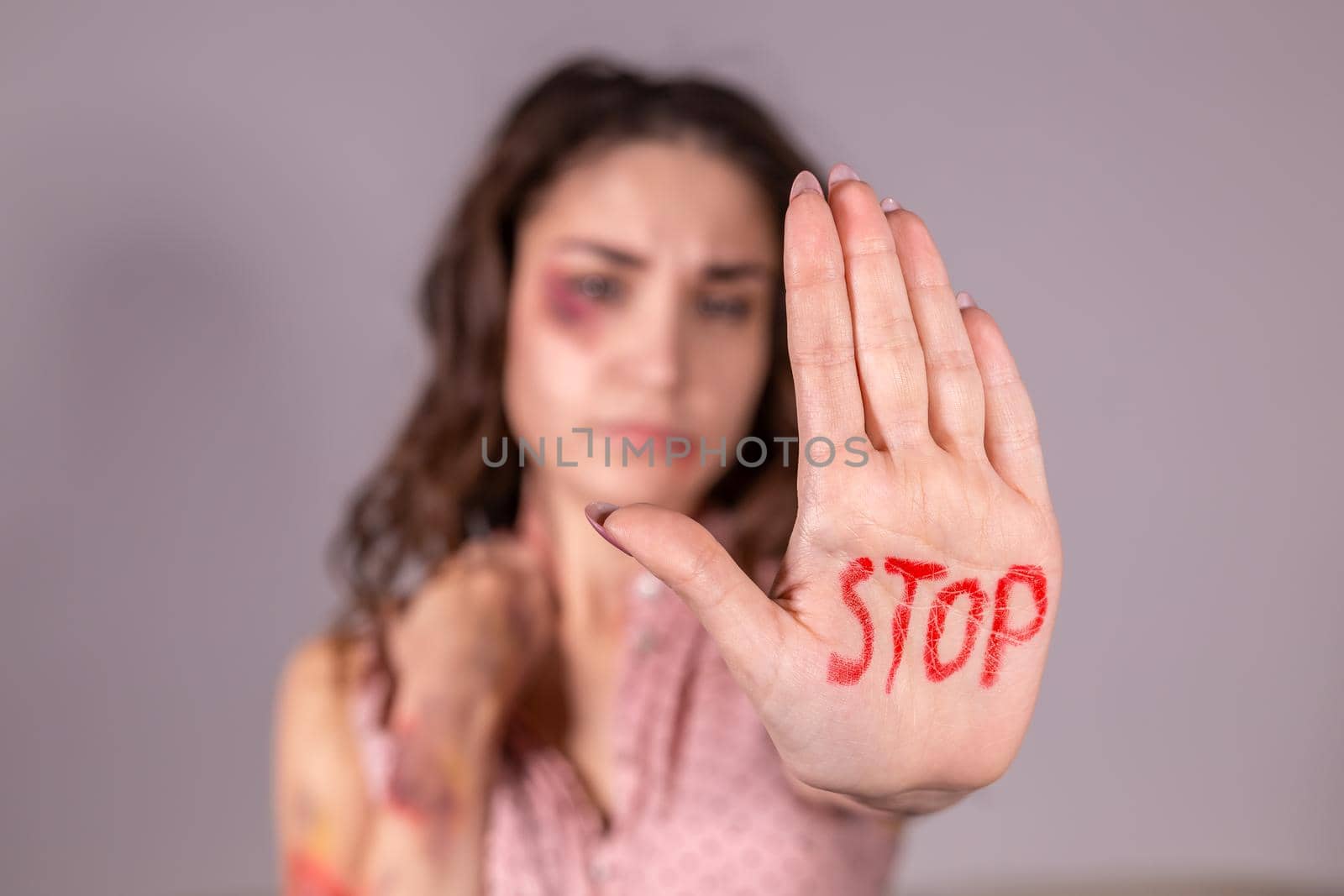 Domestic violence, protesting and people concept - brunette woman expressing denial with STOP on her hand on grey room.