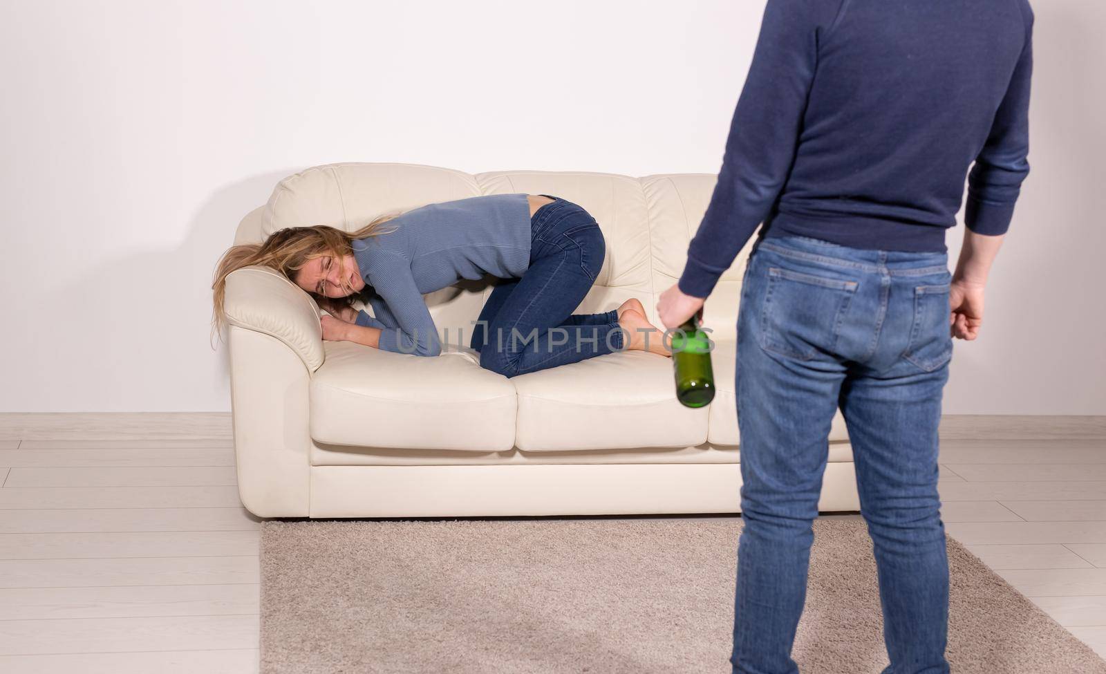 People, violence and abuse concept - Man drinking alcohol while wife is lying on sofa.