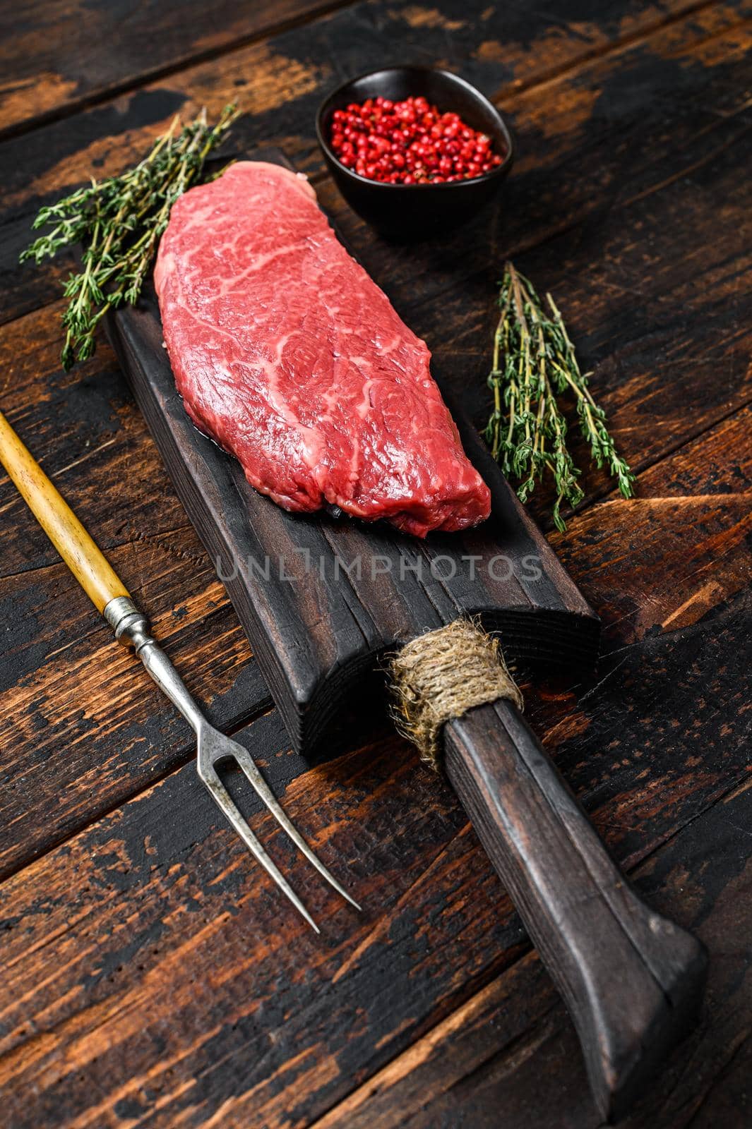 Raw Striploin steak on a cutting board, marbled beef. Dark Wooden background. Top view.