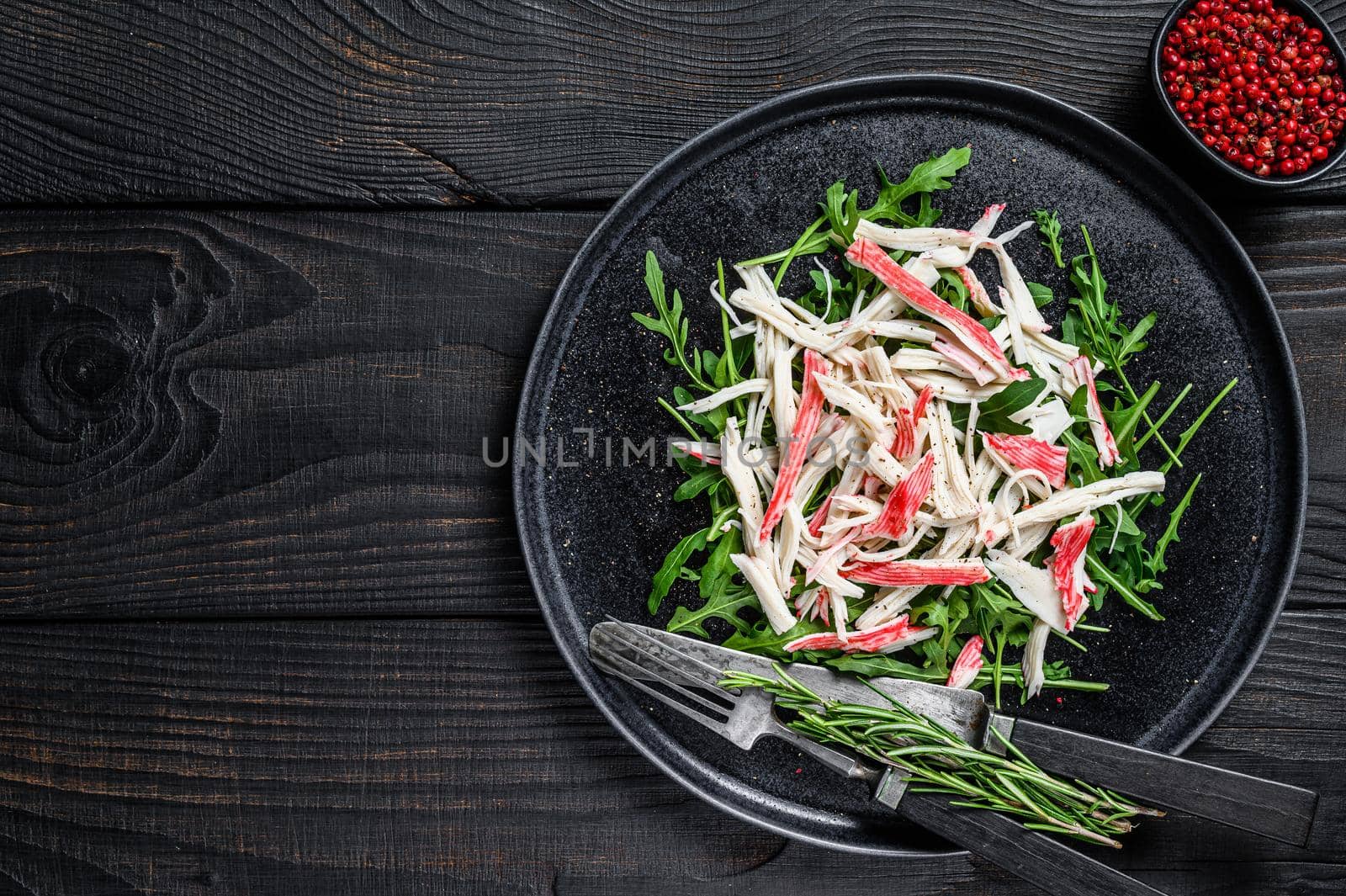 Crab meat on a plate with arugula. Black background. Top view. Copy space.