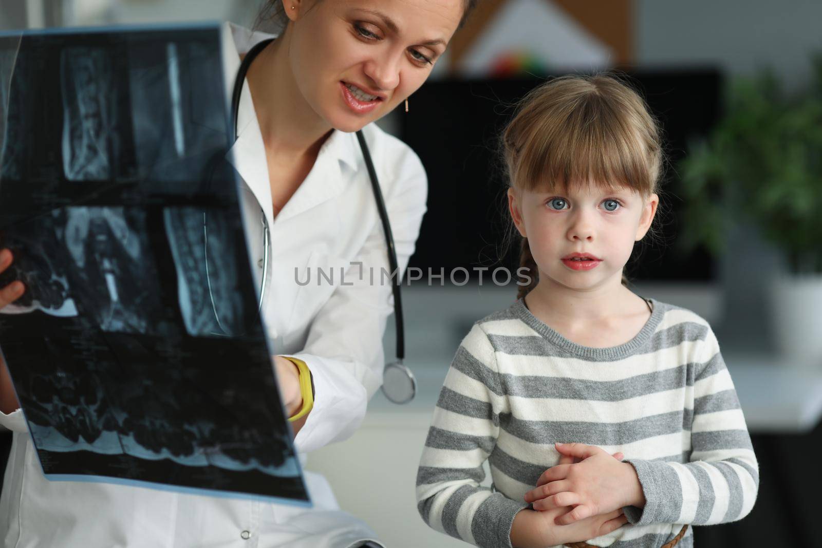 Portrait of cute woman doctor showing and explaining to daughter x ray result. Child visit mum at work in hospital. Medicine, childhood, parenthood concept