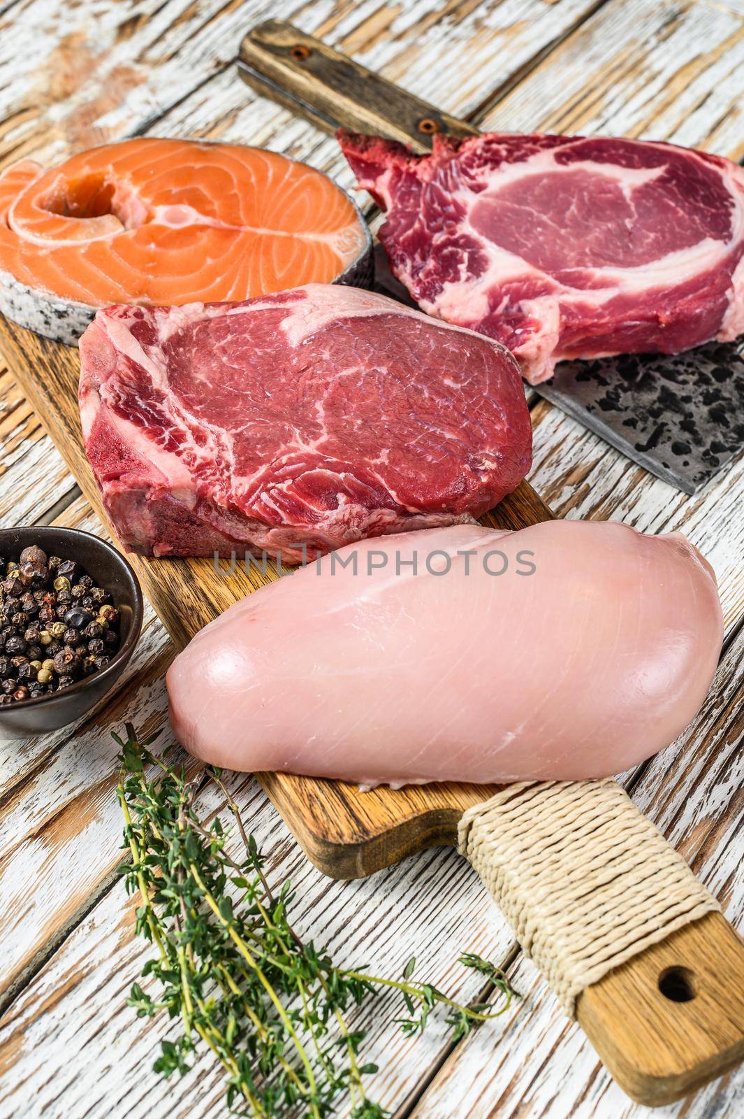 Fresh raw beef striploin steak, chicken breast fillet, pork and salmon steak. White wooden background. Top view.
