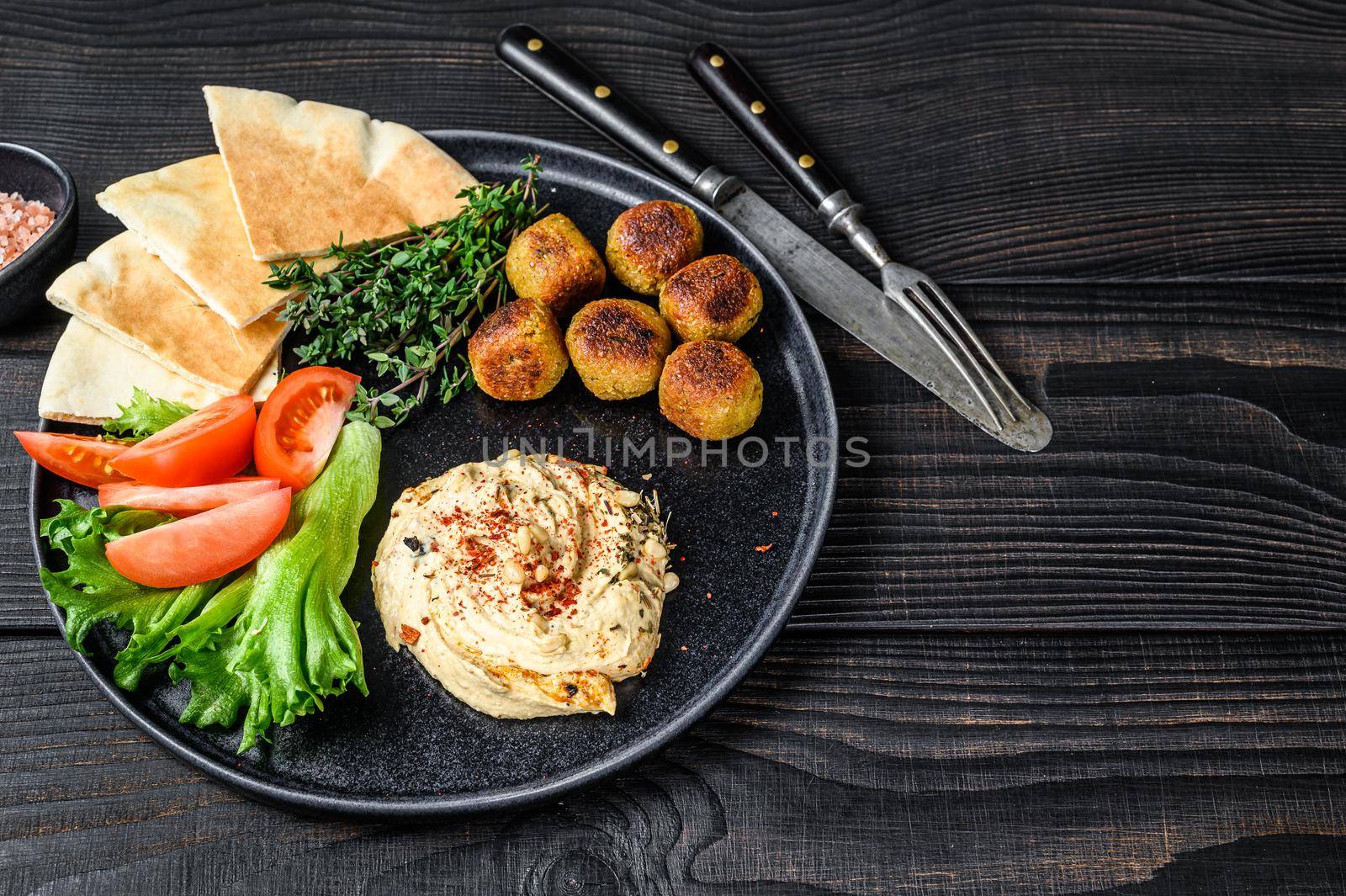 Arabic cuisine Hummus chickpea, falafel, pita bread and fresh vegetables. Black wooden background. Top view. Copy space by Composter