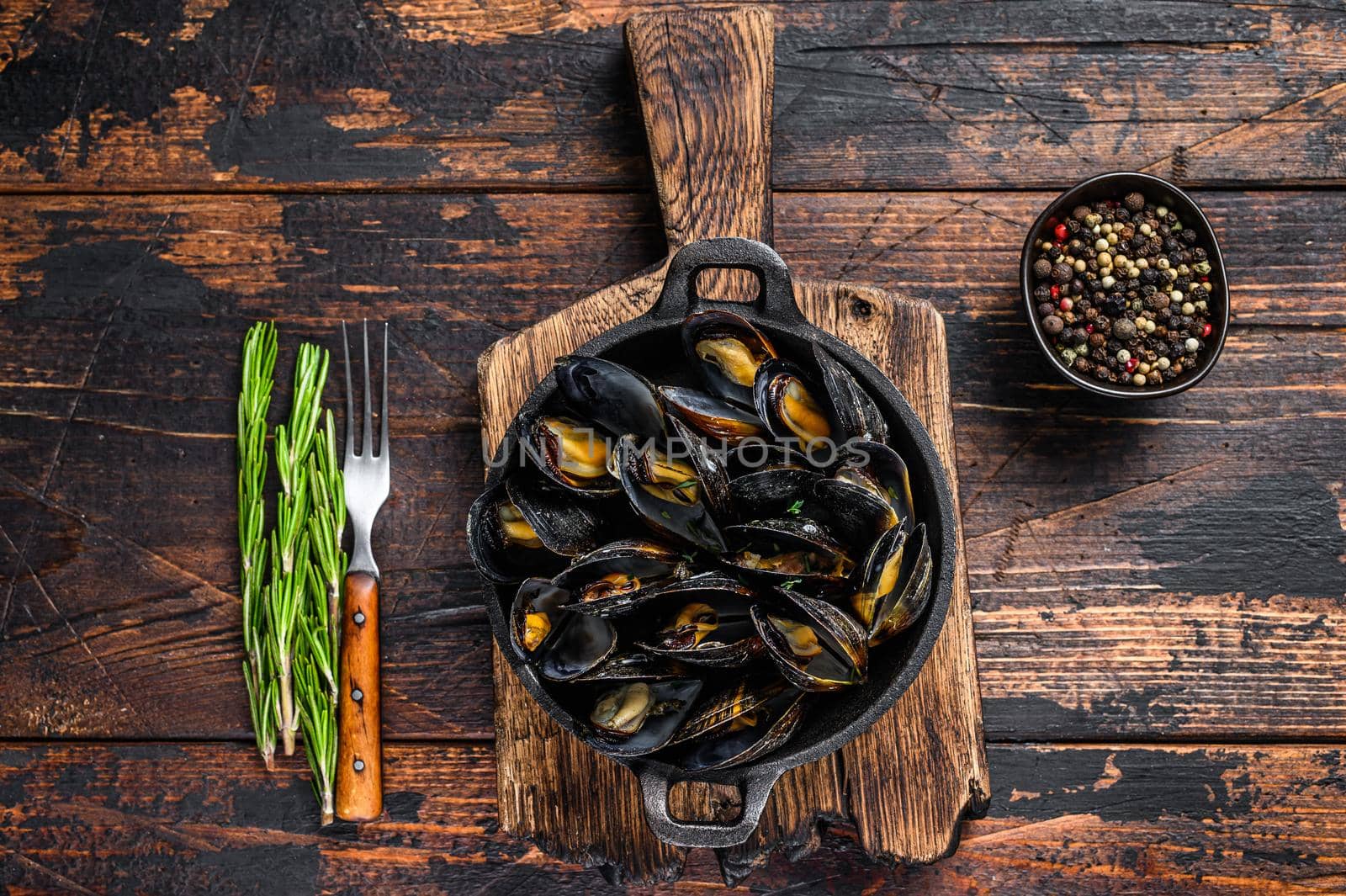 Mussels cooked with white wine sauce in a pan with herbs. Dark wooden background. Top view.