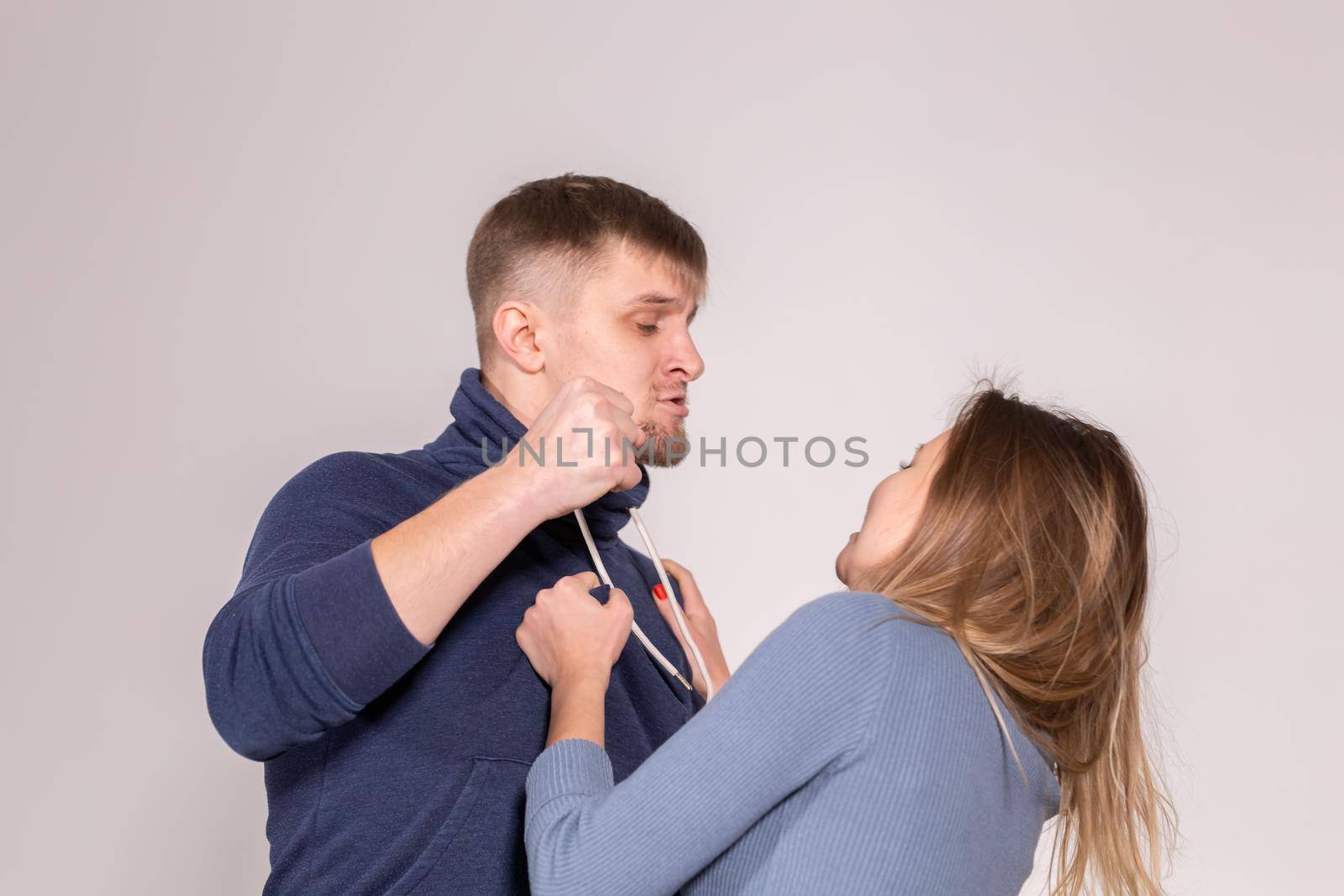 people, domestic violence and abuse concept - young man threatens his wife with his fist on white background.