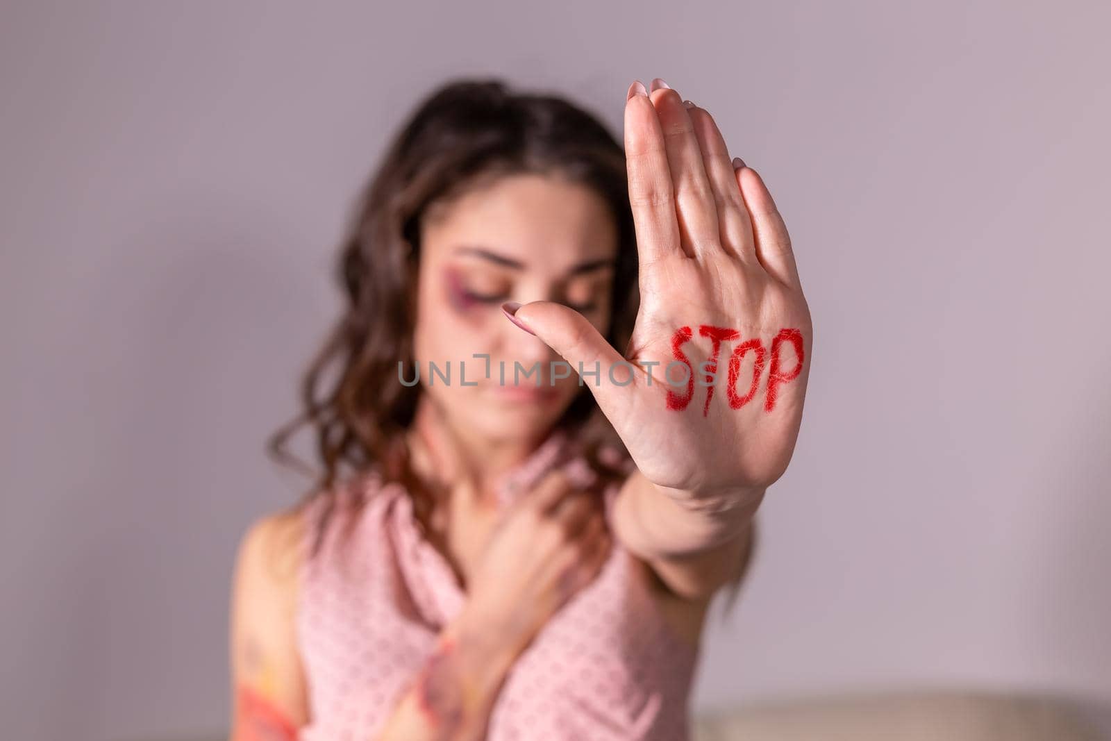 Domestic violence, protesting and people concept - brunette woman expressing denial with STOP on her hand on grey room.