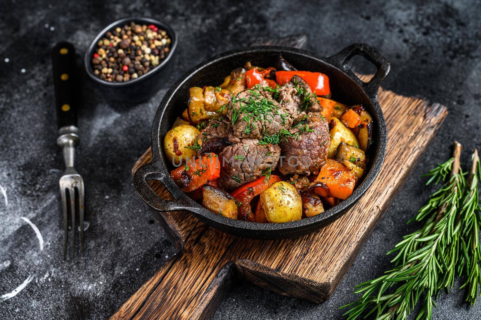 Meat stew in cooking pot on dark rustic cutting board. Black background. Top view by Composter