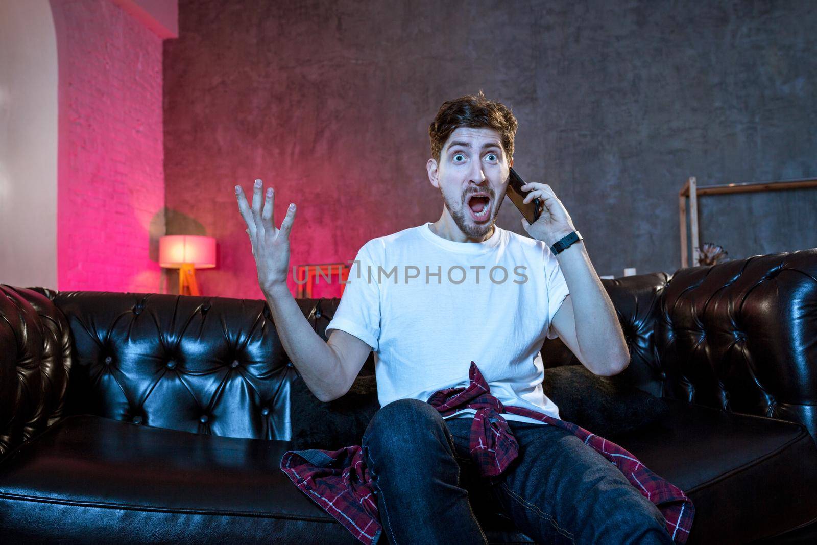 Young supporter man watching football game on television sitting at home couch with ball beer and chips in stress dejected and disappointed for failure shouting and complaining. Emotional fan watching the game of your favorite team