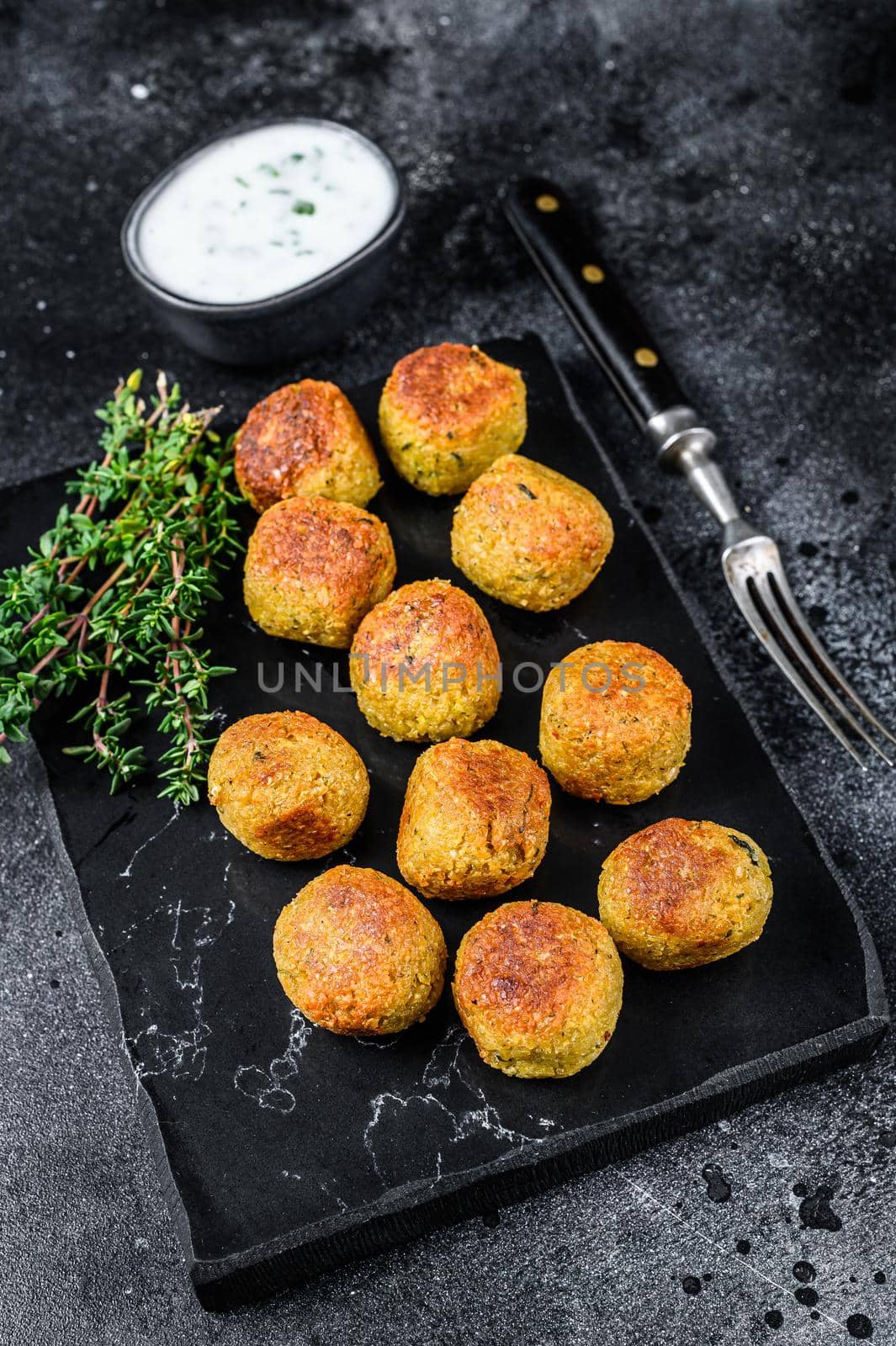 Roasted vegetarian falafel balls from spiced chickpeas with garlic yogurt sauce. Black background. Top view.