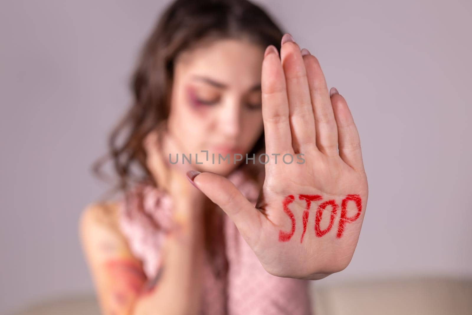 Domestic violence, protesting and people concept - brunette woman expressing denial with STOP on her hand on grey room.