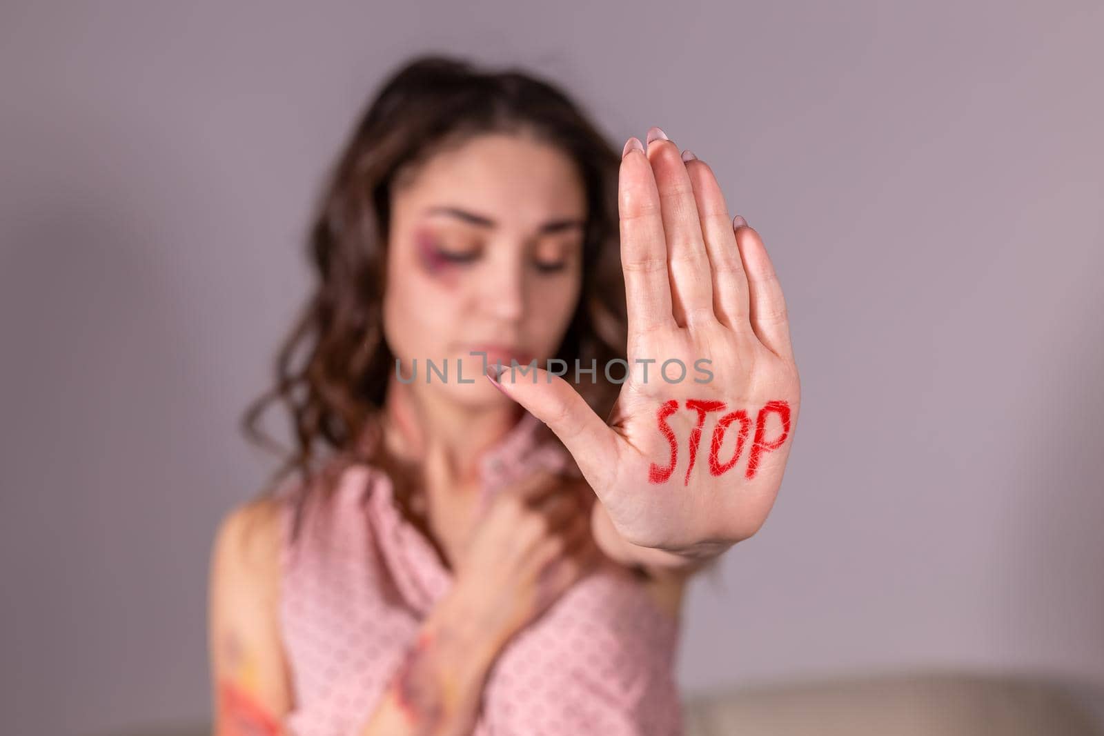 Domestic violence, protesting and people concept - brunette woman expressing denial with STOP on her hand on grey room.