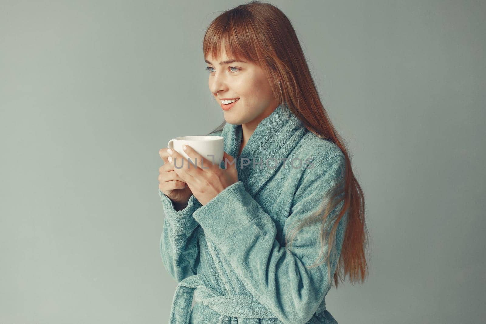 Girl in a studio. Lady in a blue bathrobe. Woman drinking a coffee