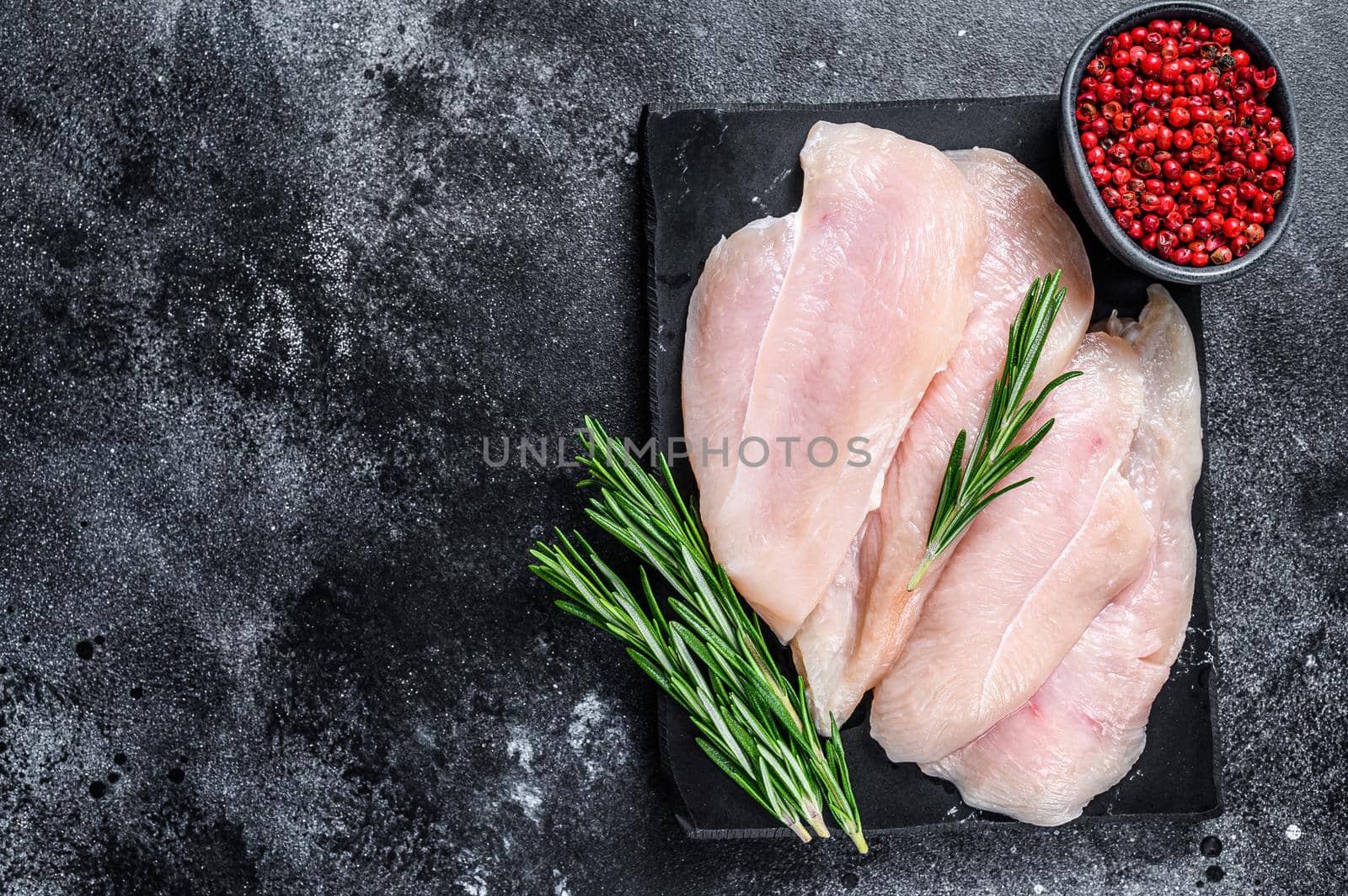 Raw sliced chicken breast fillet steaks on a marble board. Black background. Top view. Copy space.