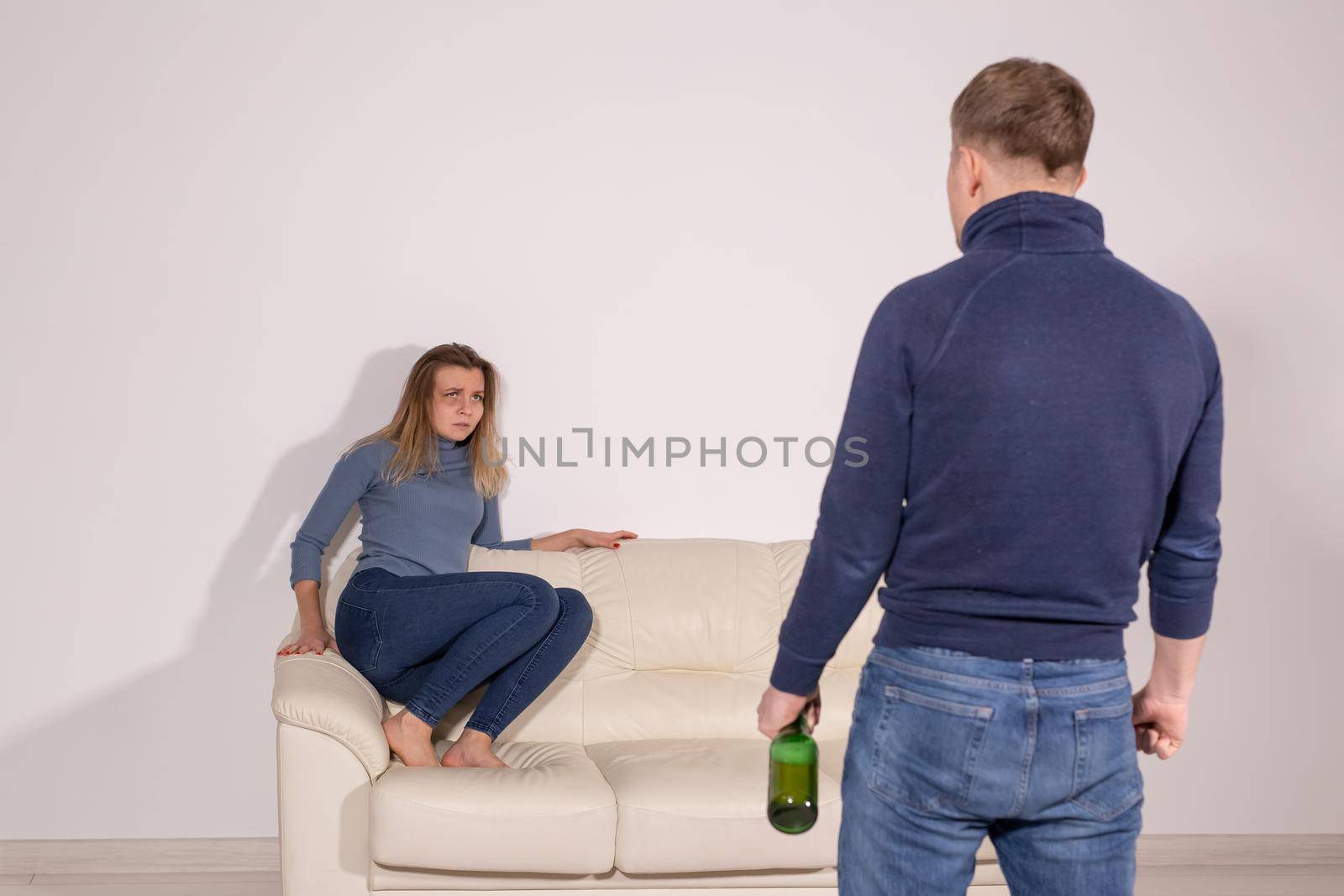 People, violence, alcoholism and abuse concept - Man with bottle alcohol while wife is lying on sofa.