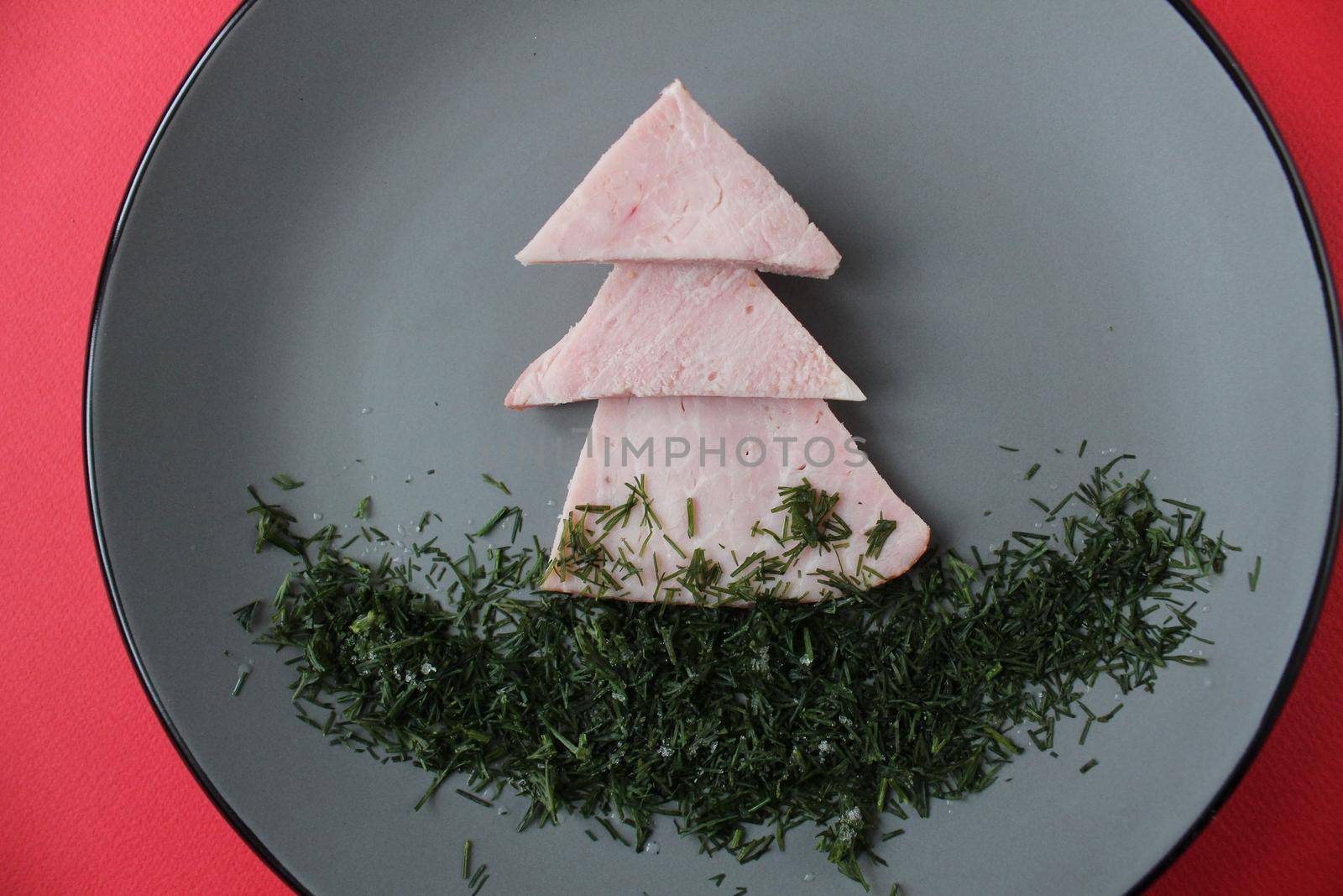 edible Christmas tree and sausages on a gray plate on a red background with a branch of a Christmas tree. A place for copyspace for text. Funny children's food.