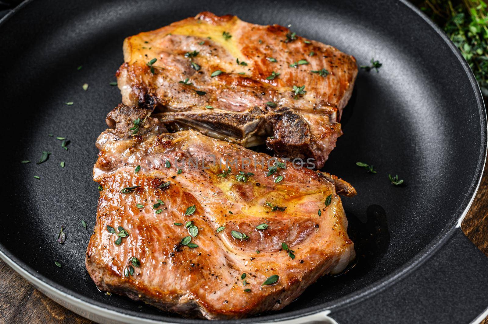 Fried pork loin steaks in a pan. Dark wooden background. Top view.